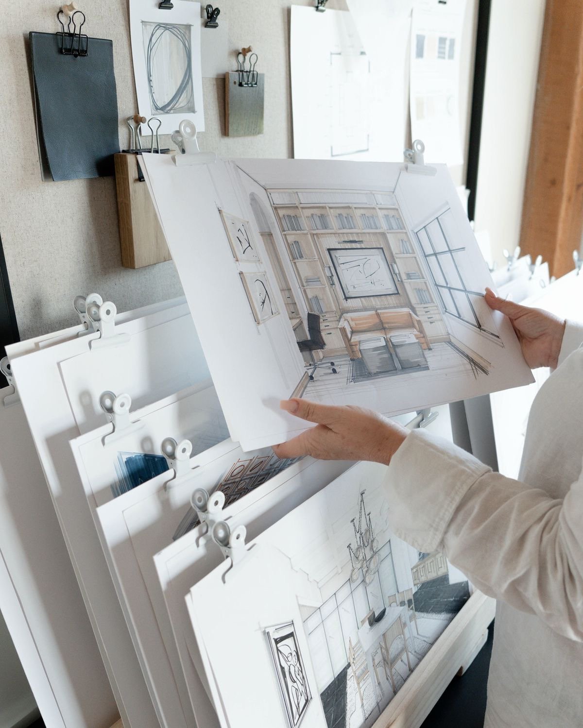 Person holding interior design sketches with furniture and room layouts.