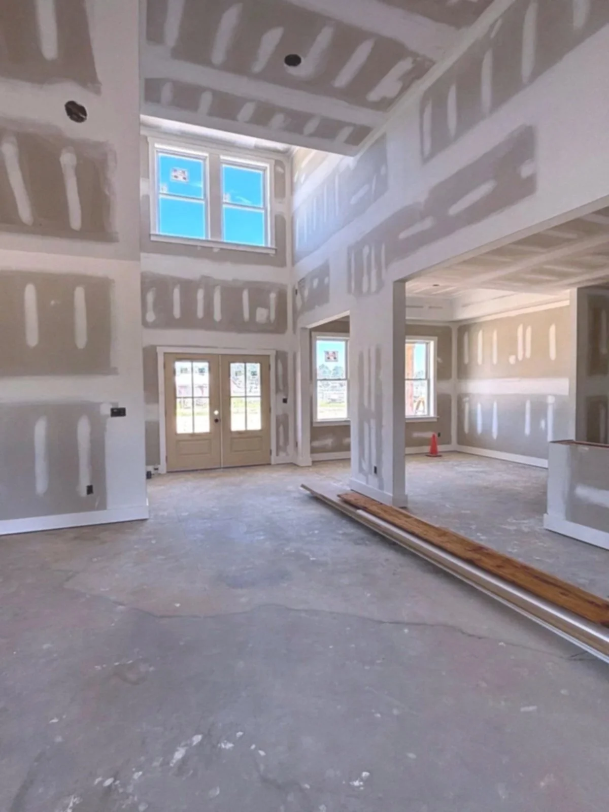 Interior view of a house under construction, with drywall installed but not painted, and construction materials on the floor.