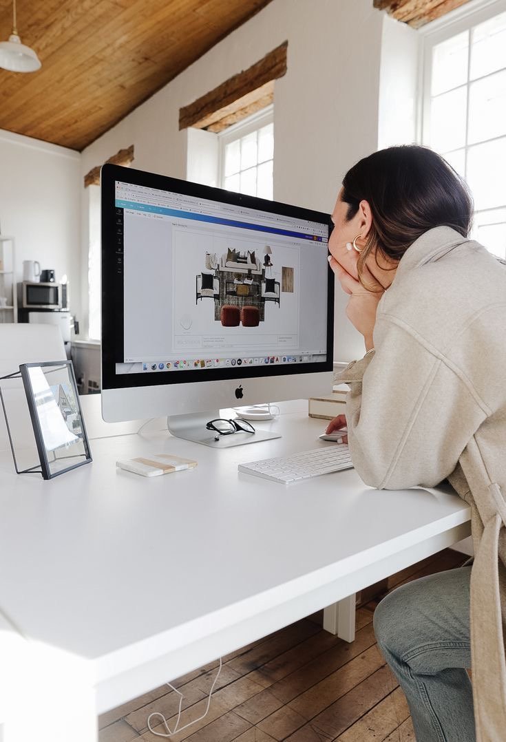 A person sitting at a white desk and looking at a computer screen displaying a home interior design layout.