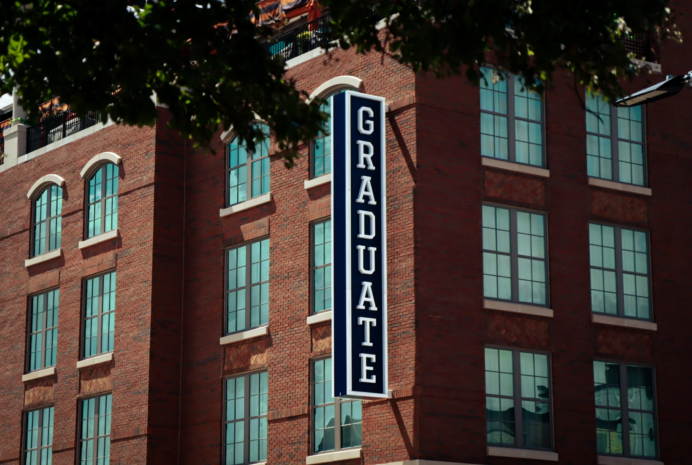 A long blue sign with the Graduate Hotel logo, displayed on the Graduate Auburn