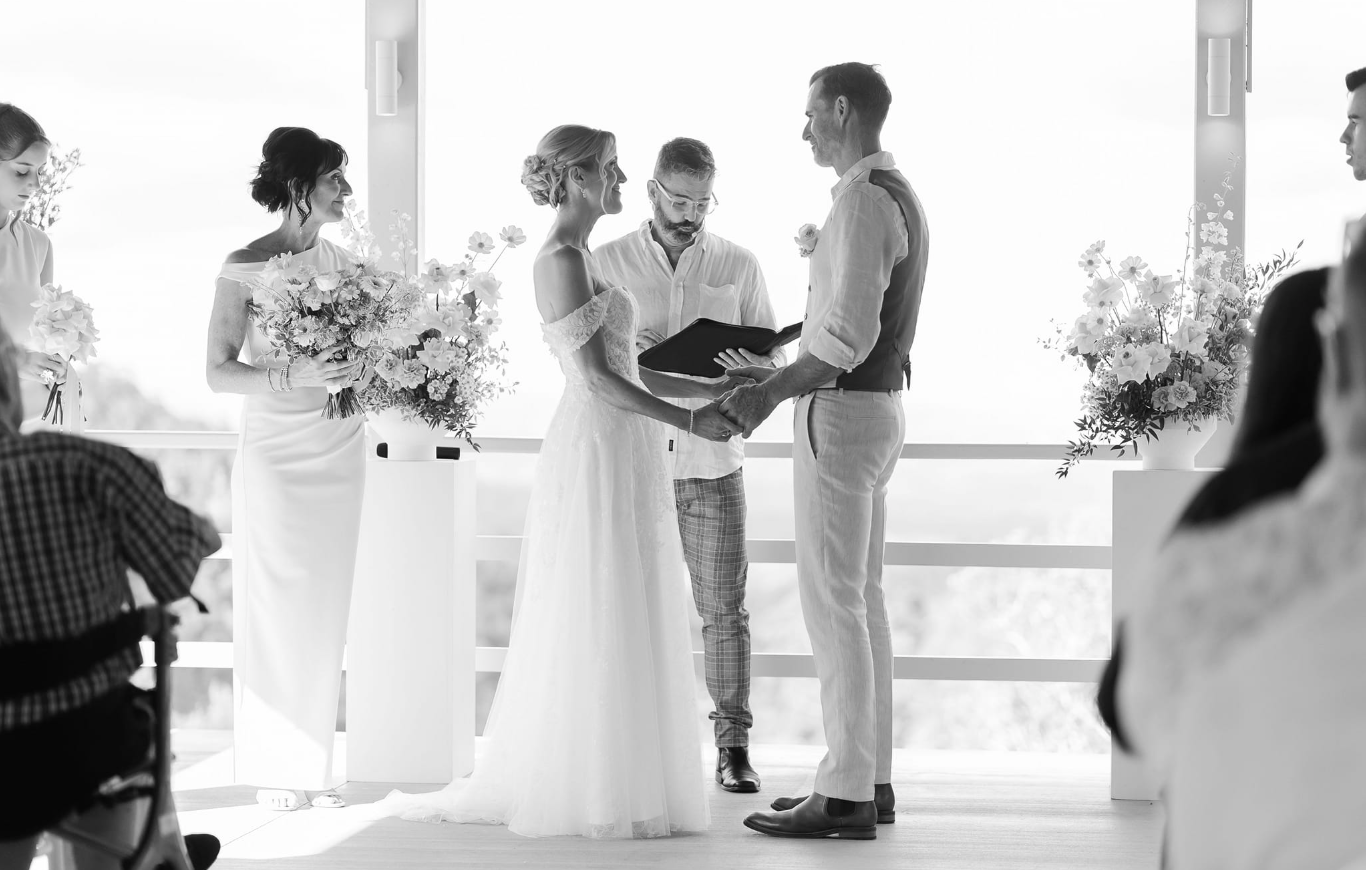 Couple holding hands during wedding ceremony with officiant, Anthony Spark and bridesmaids in background.