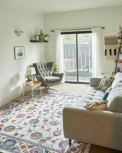 Bright living room with a gray sofa and armchair, a colorful area rug, and a sliding glass door leading to a patio.