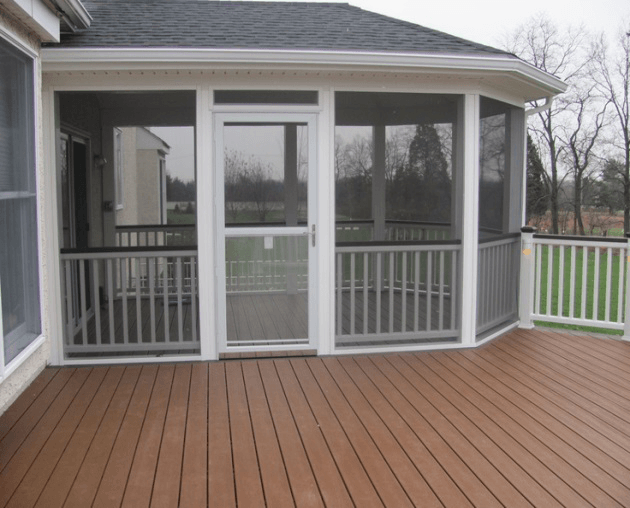 Front view of a screened porch with wooden flooring, a white door, and white railings.