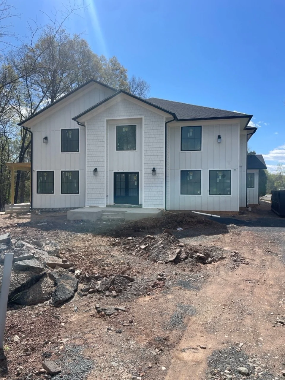 Newly constructed white two-story house with multiple windows and a front porch, surrounded by a dirt and gravel yard under a clear blue sky.