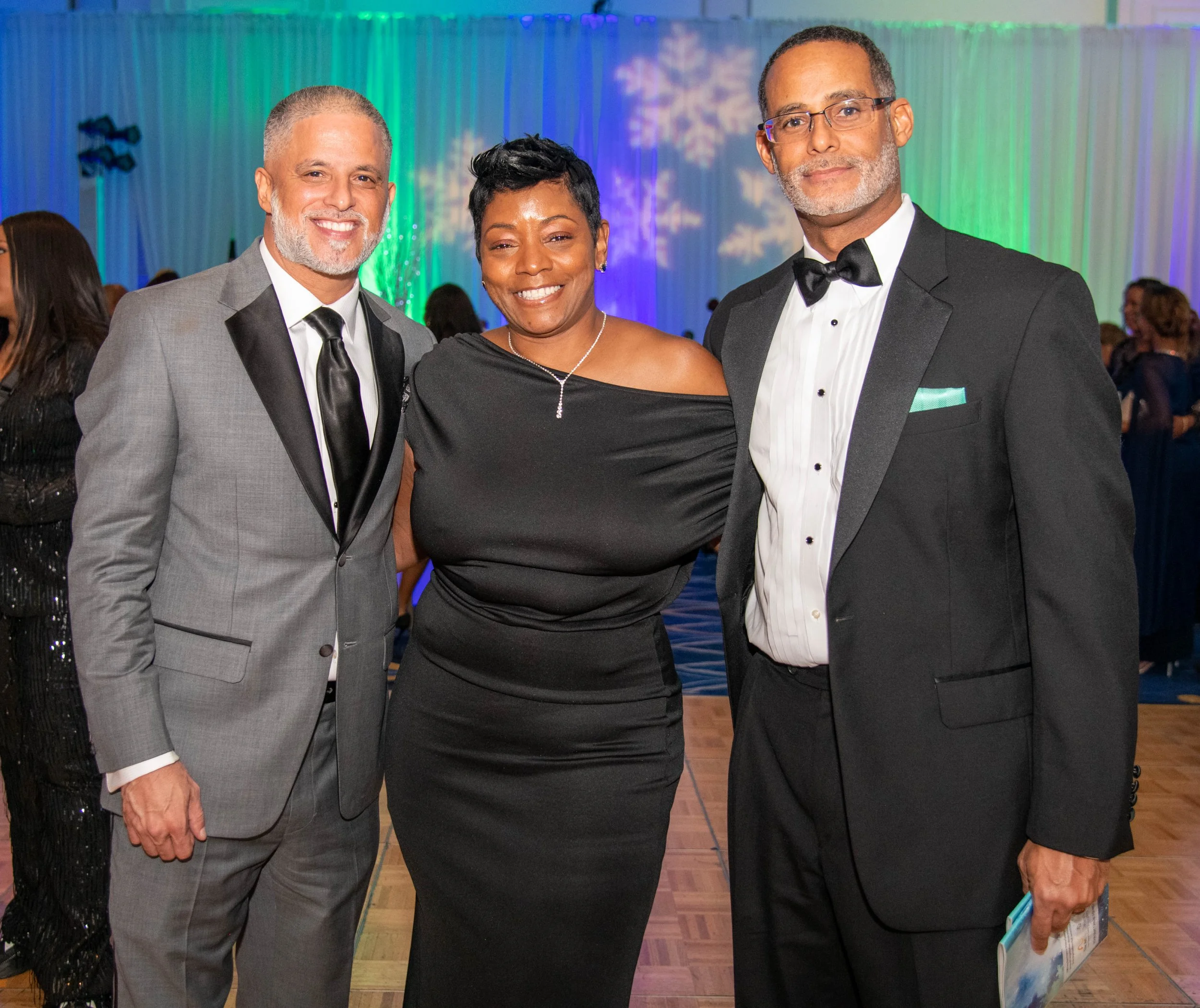 Three adults in formal attire standing together at an event with colorful background