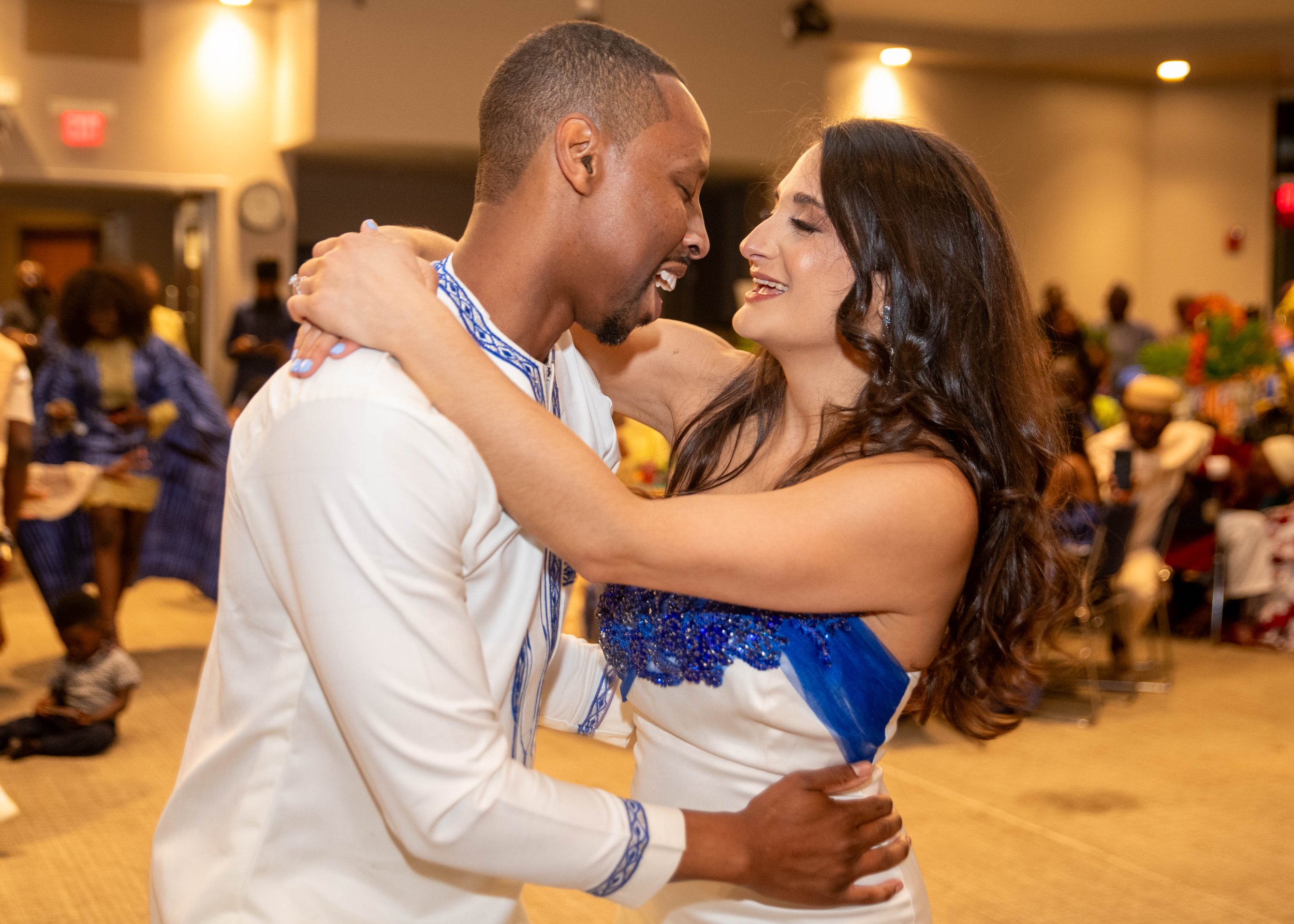 A couple dancing closely and smiling at each other in a warm, lively indoor setting.
