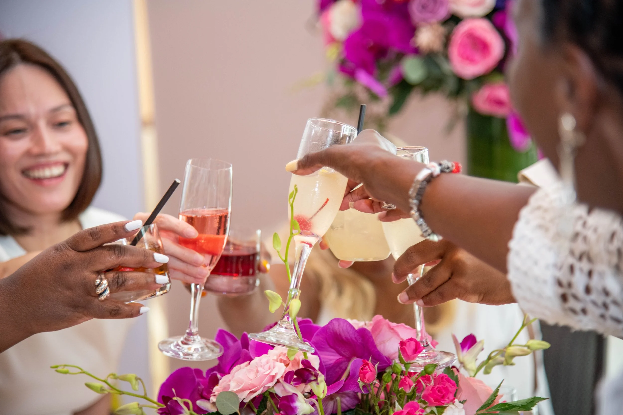 Women raising glasses in toast at a celebration with pink and purple flower arrangement in the foreground.