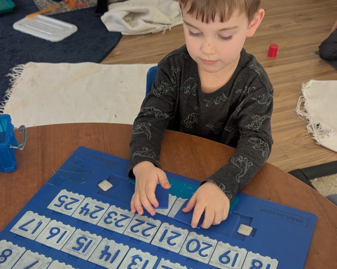 A young boy playing with a number puzzle on a round wooden table indoors.