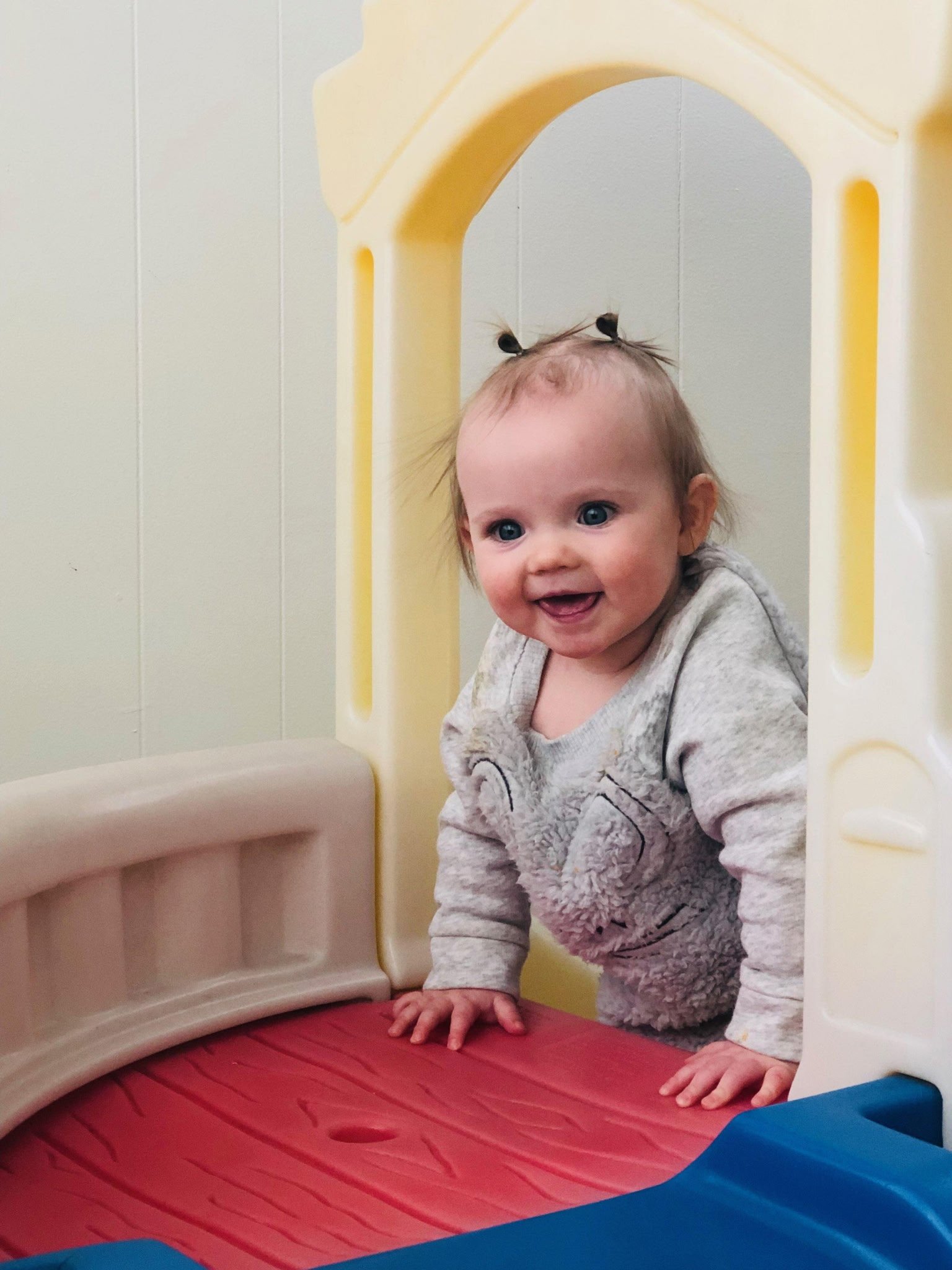 Smiling baby with pigtails in a playhouse.