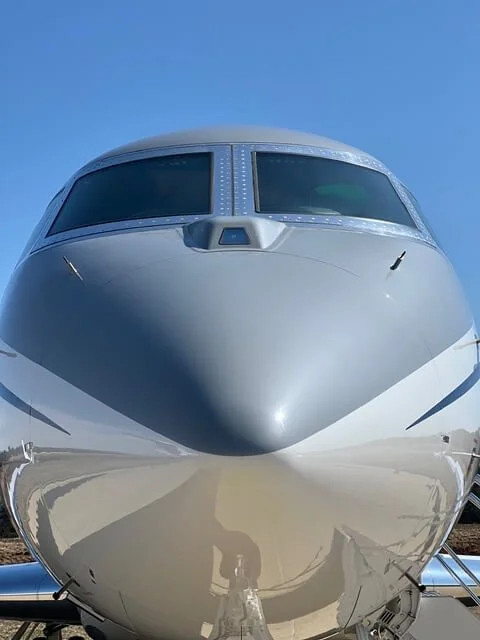 Front view of a white private jet airplane on the tarmac under a blue sky.