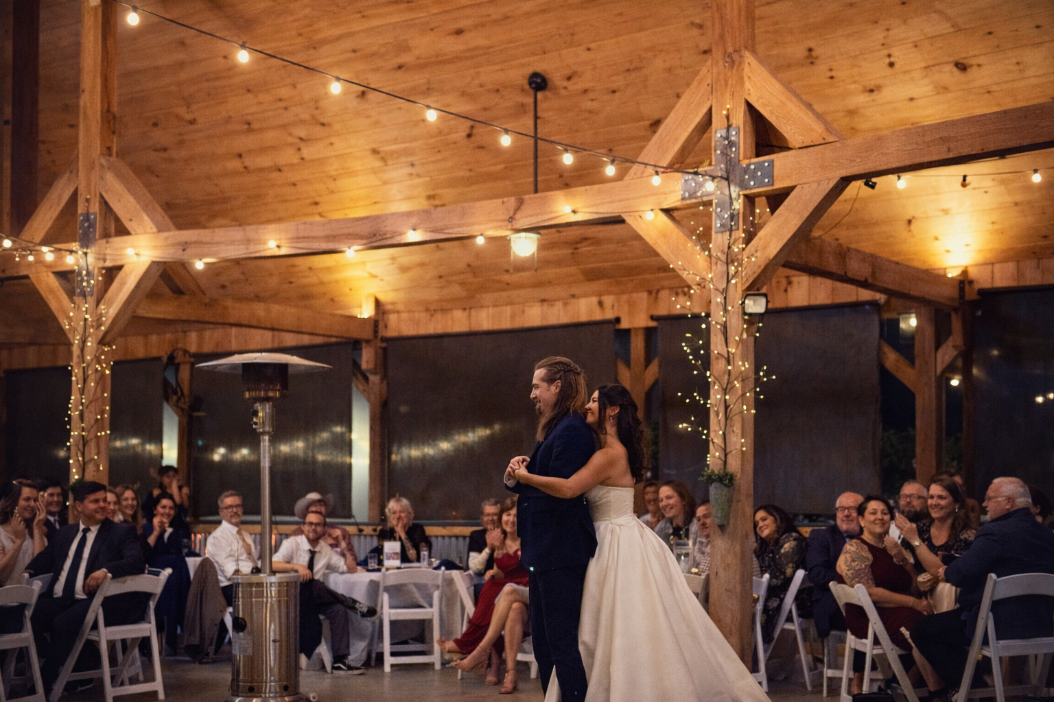 Bride and groom dancing together beneath wooden beams and string lights at a Chapel Hill venue.