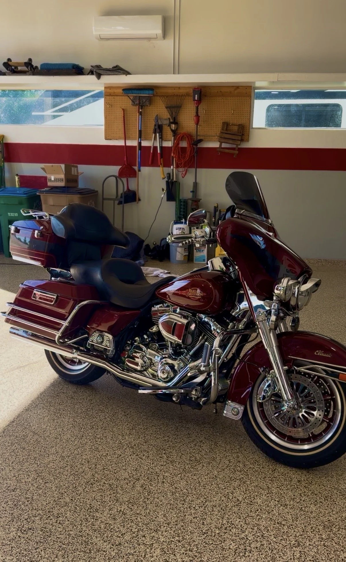 A burgundy Harley Davidson motorcycle parked indoors, with a garage wall and tool rack in the background.