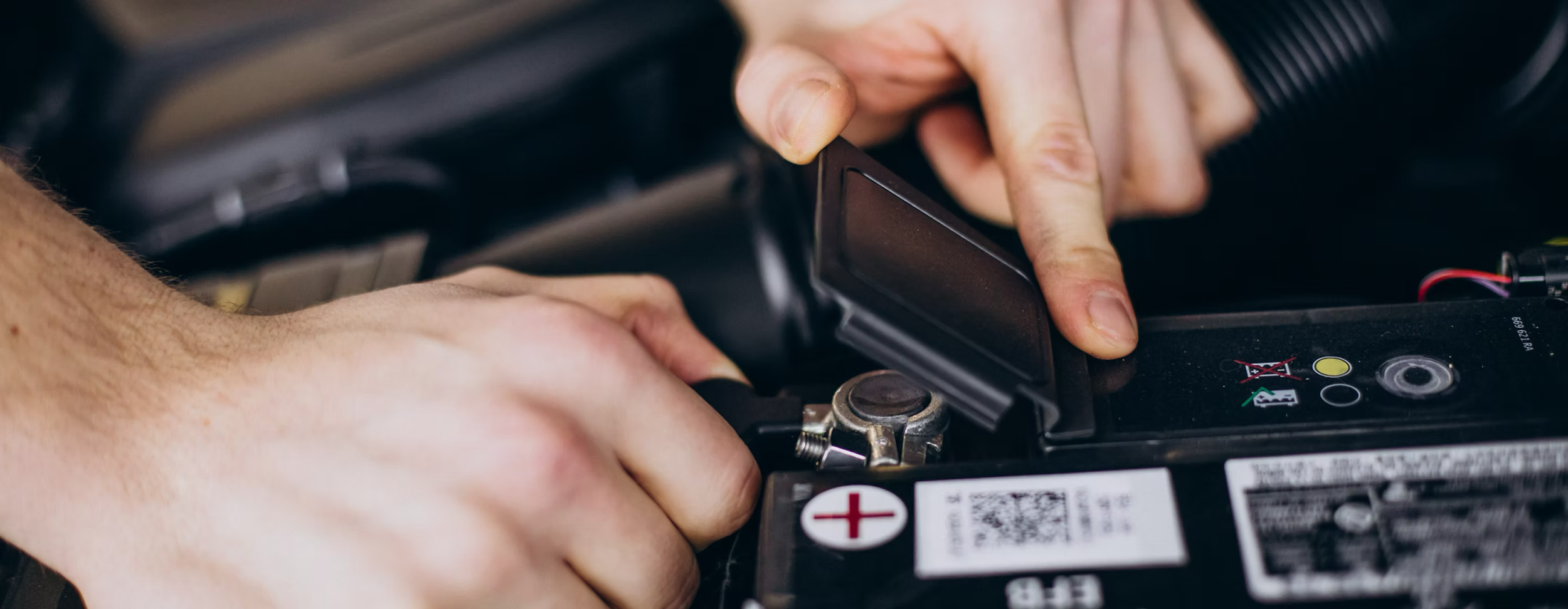 Person working on car battery, handling black plastic cover, in a close-up view.