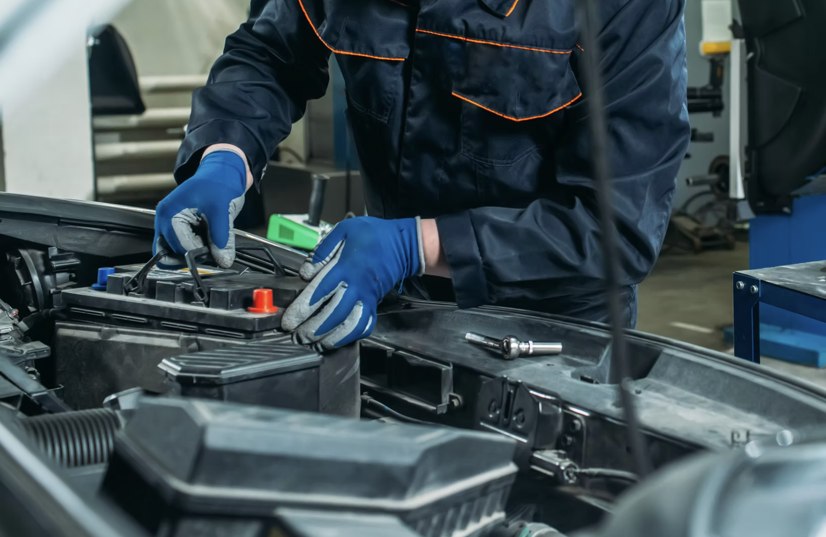 A mechanic wearing blue gloves working on a car battery in an auto repair shop.