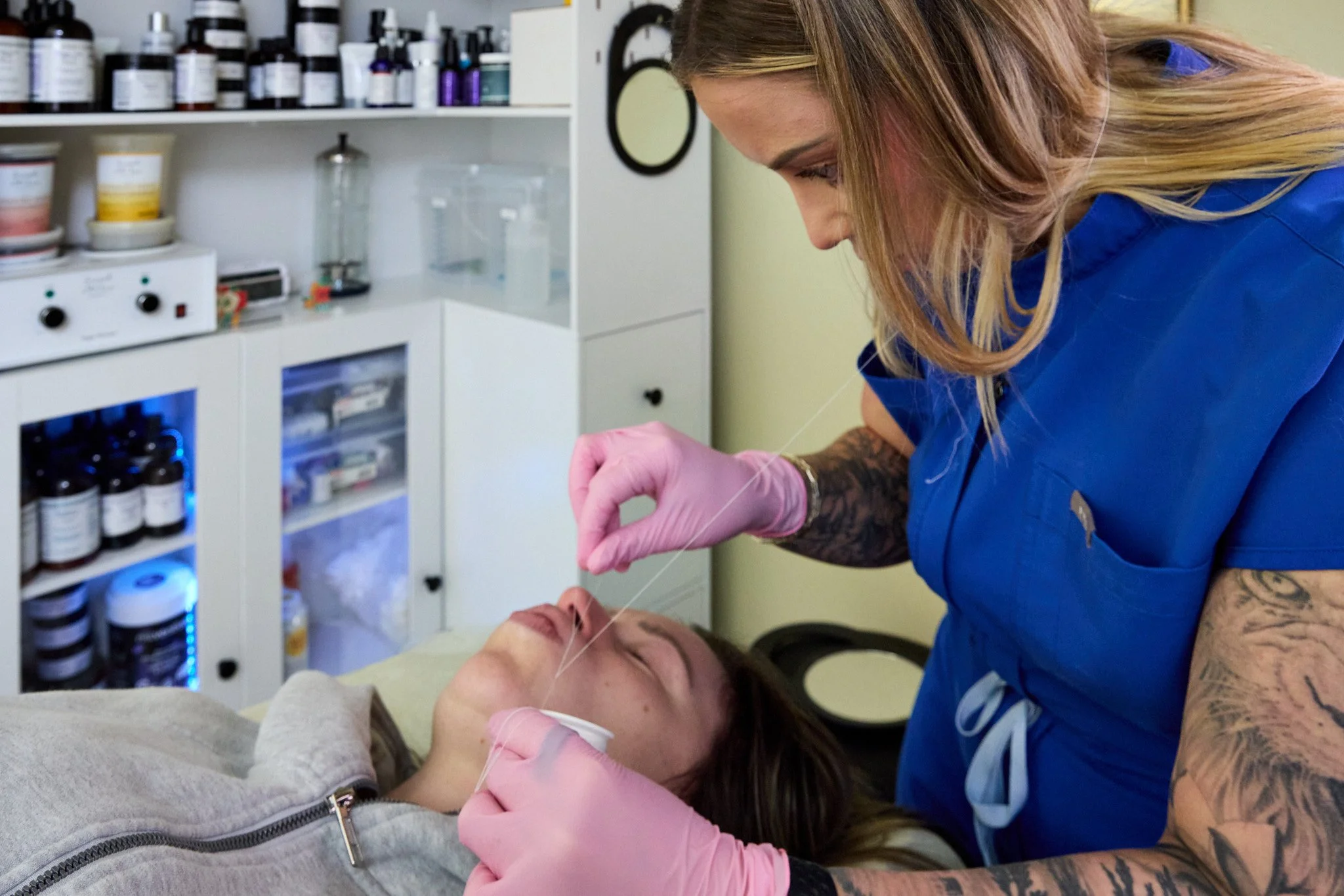 Rachel, in blue scrubs and pink gloves, is cleaning a client's face, post-treatment.