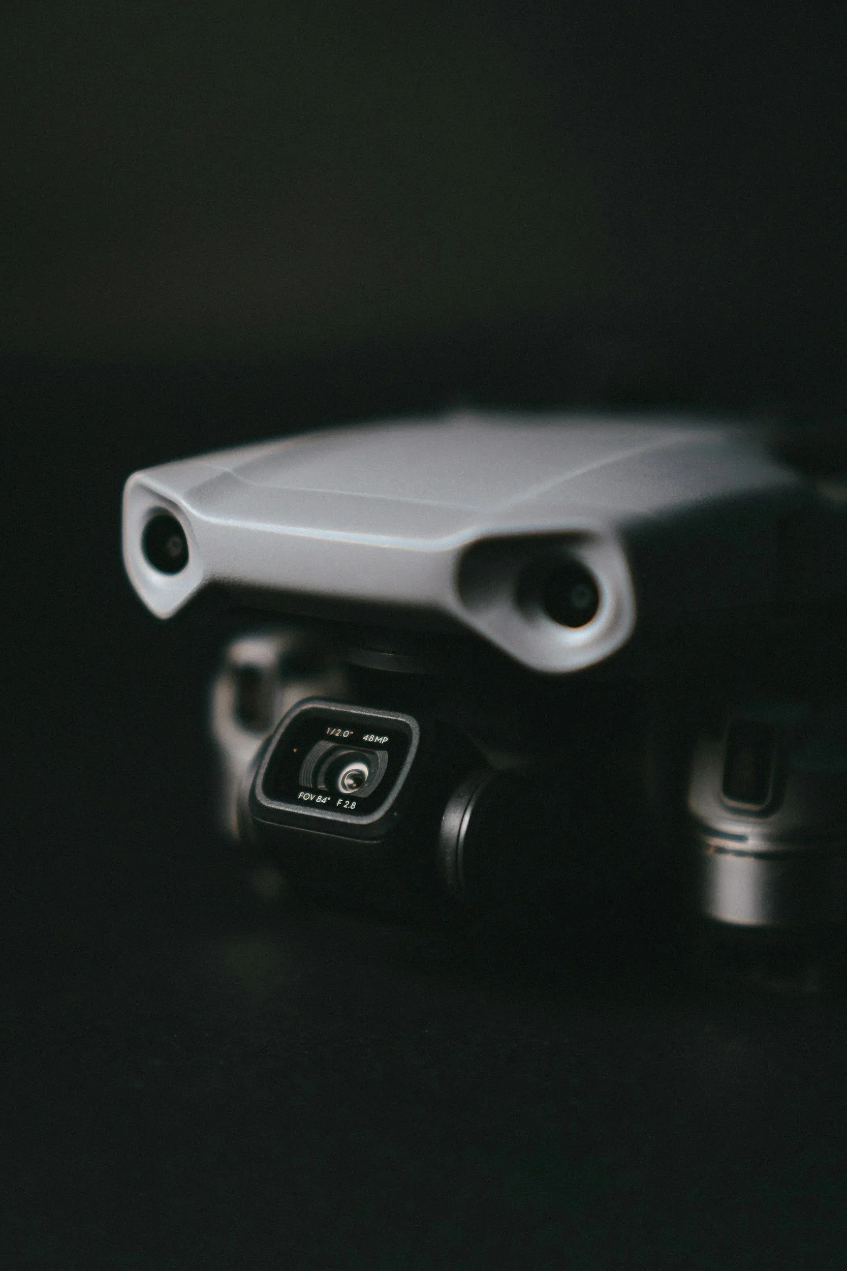 Un drone blanc posé sur un fond noir, avec une caméra sous son corps.