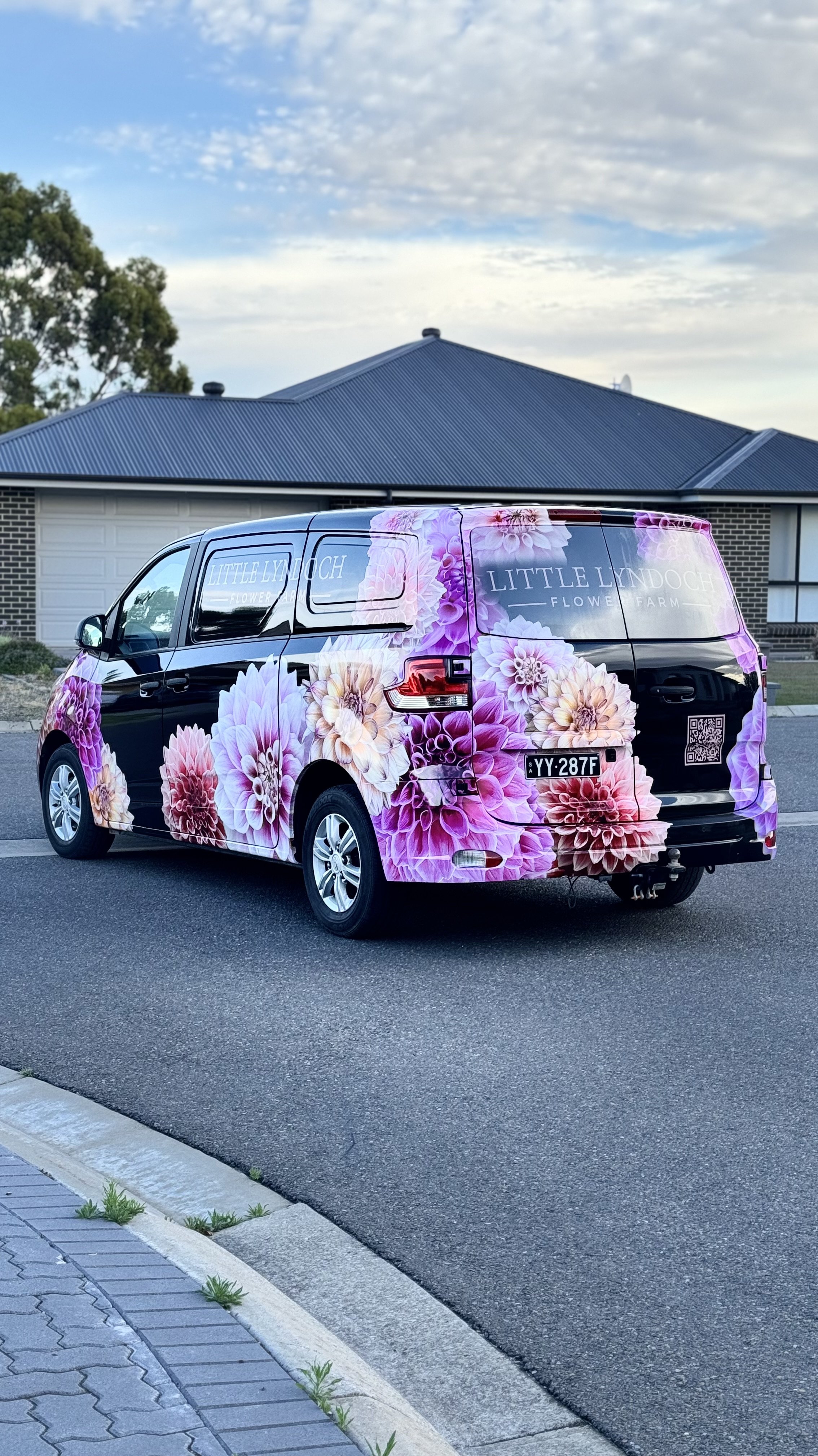 A black van with floral wrap advertising Little Lyndoch Flower Farm parked on a residential street.
