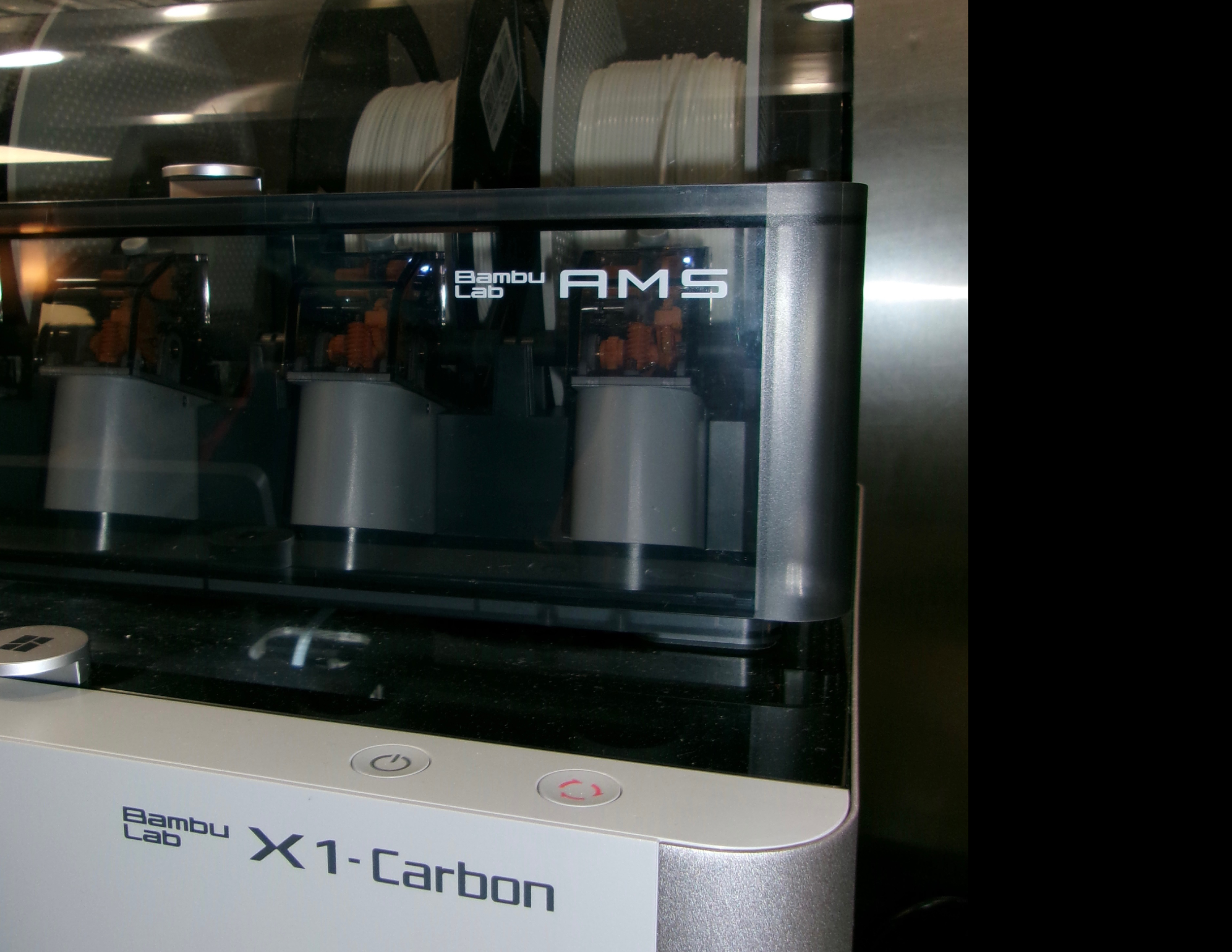 A Bambui Lab X1-Carbon 3D printer with the cover closed, showing the interior mechanics and filament spools inside.