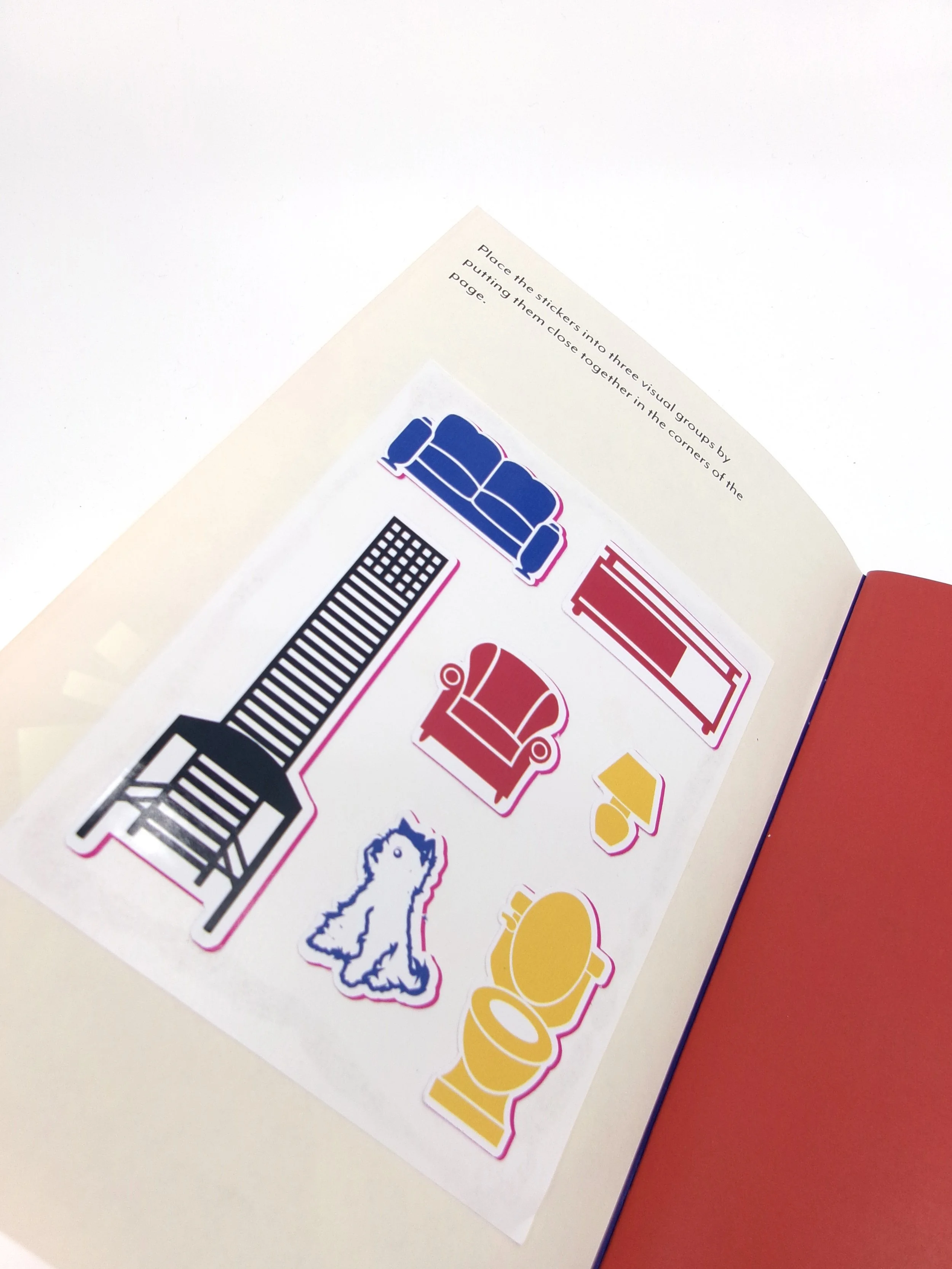 Colorful stickers of a couch, armchair, fireplace, rug, lamp, dog, and toilet on a white sheet of paper, with crafting instructions at the top.