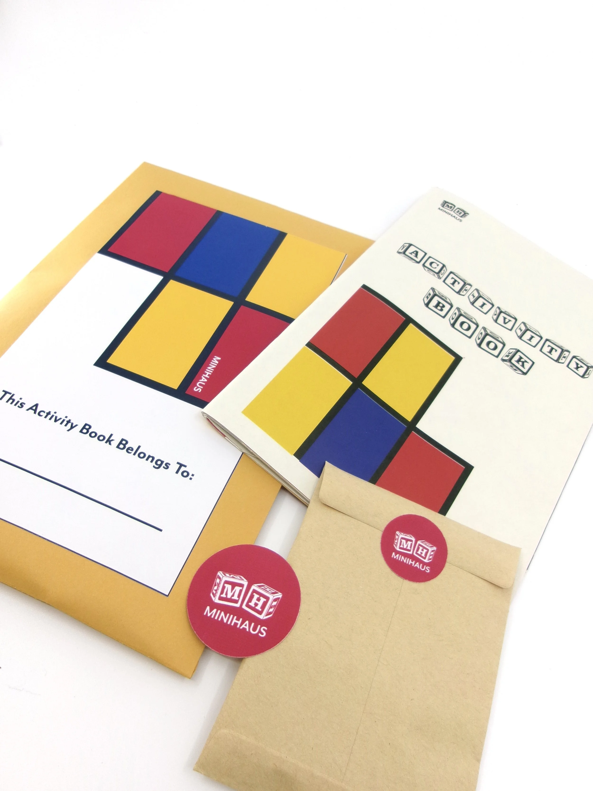 Colorful activity book and booklet with geometric patterns, stickers, and a small brown envelope on a white surface.