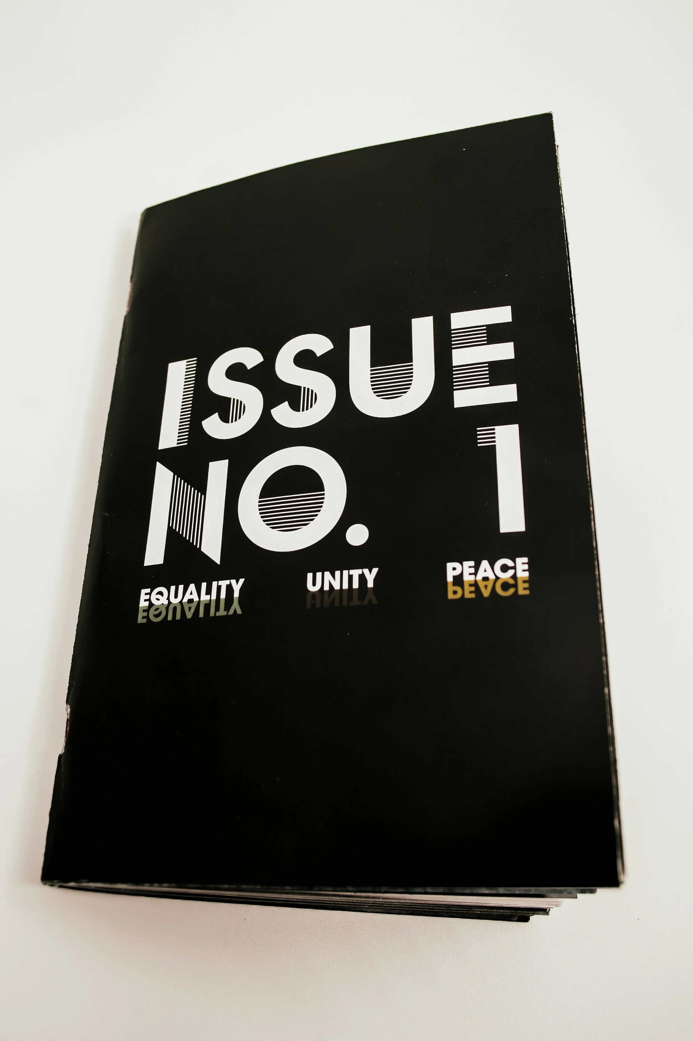 A black booklet or magazine with the title 'Issue No. 1.' The cover features the words 'Equality,' 'Unity,' and 'Peace' at the bottom.
