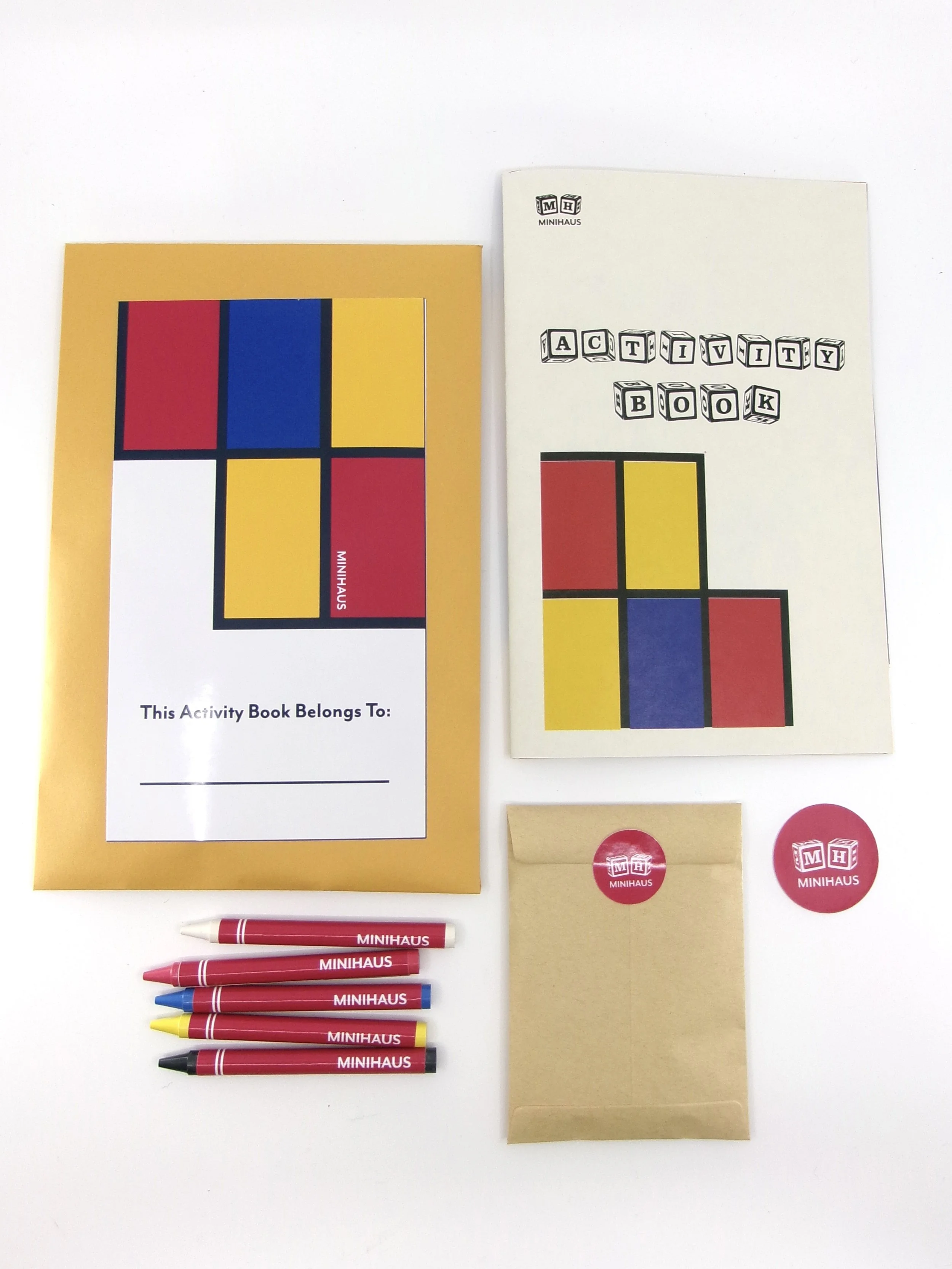 Set of MiniHaus activity book, pen, markers, stickers, and paper bag on a white background. The activity book has a cover design inspired by De Stijl and the Bauhaus with red, blue, yellow, black, and white blocks.