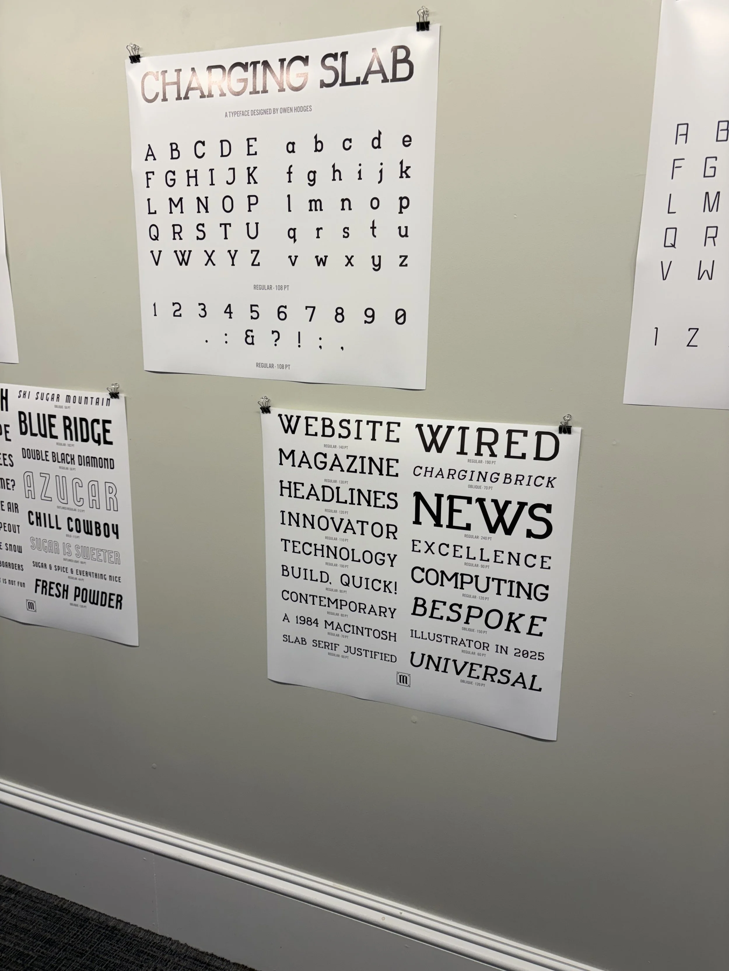 Posters on a wall featuring different fonts and typefaces, including a 'Charging Slab' font chart designed by Owen Hodges.