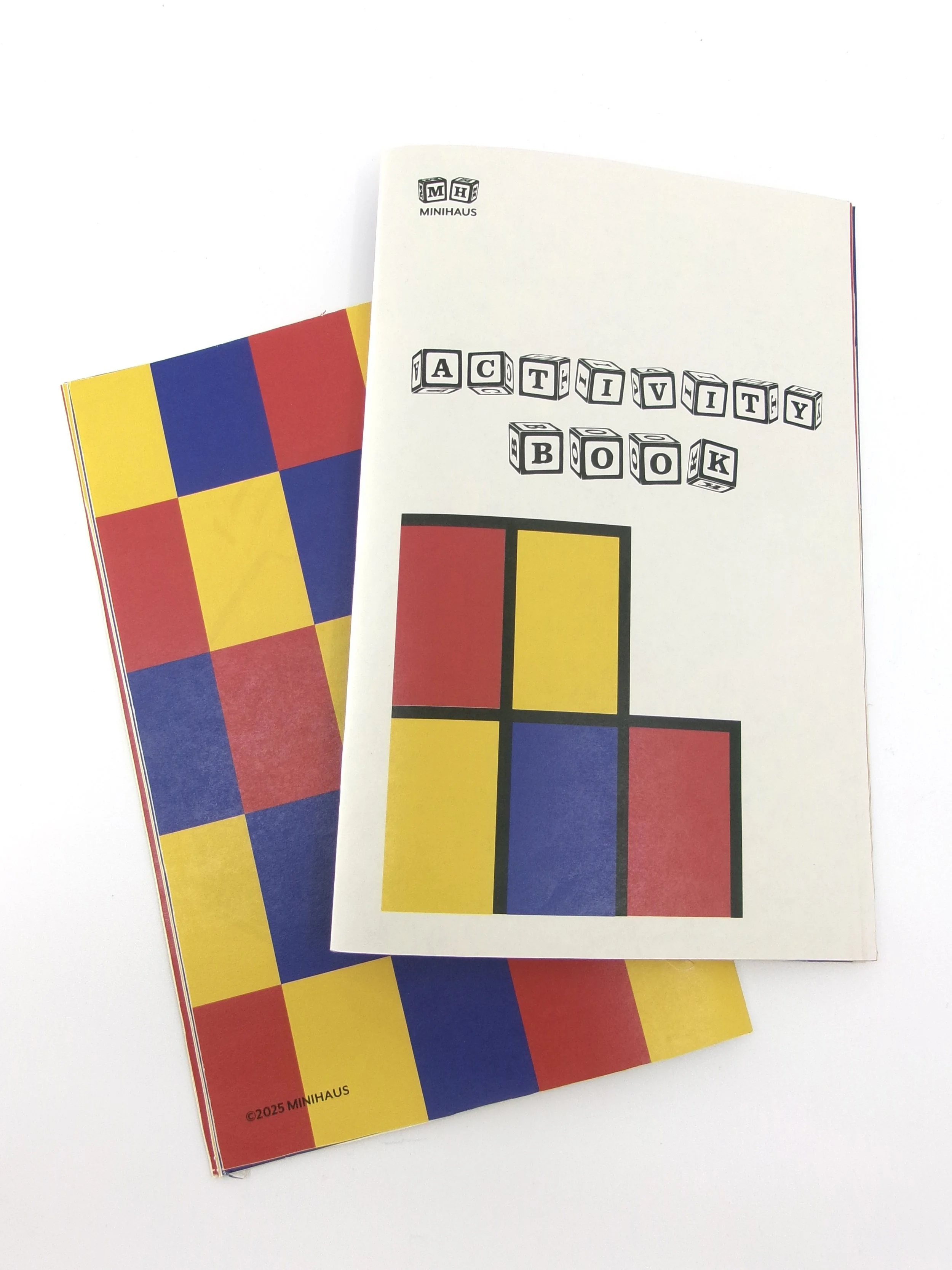 A colorful activity book with a red, yellow, and blue cover, and a white activity booklet on top featuring geometric shapes and the words 'Activity Book' in block letters.