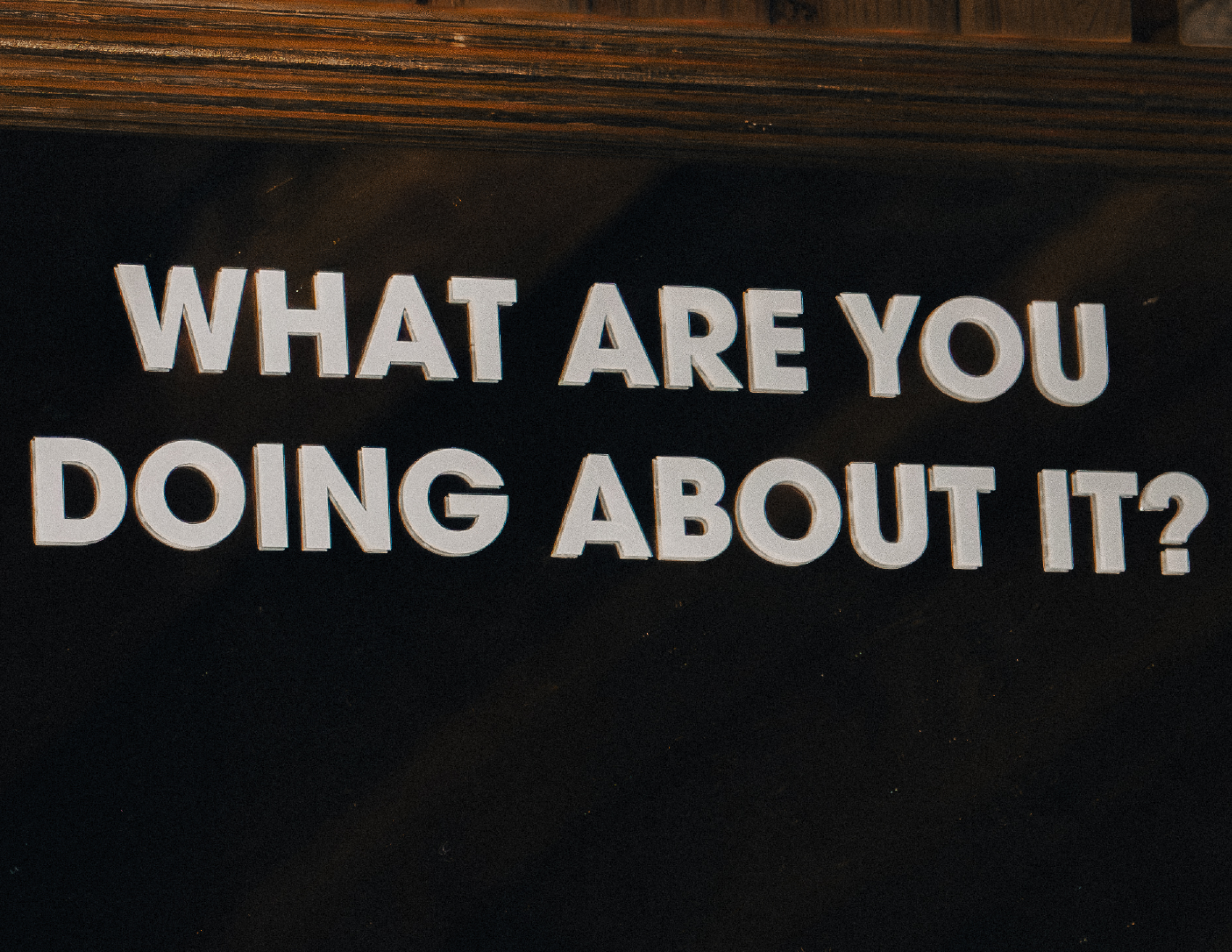 A sign with the text "What are you doing about it?" in large white letters on a black background.