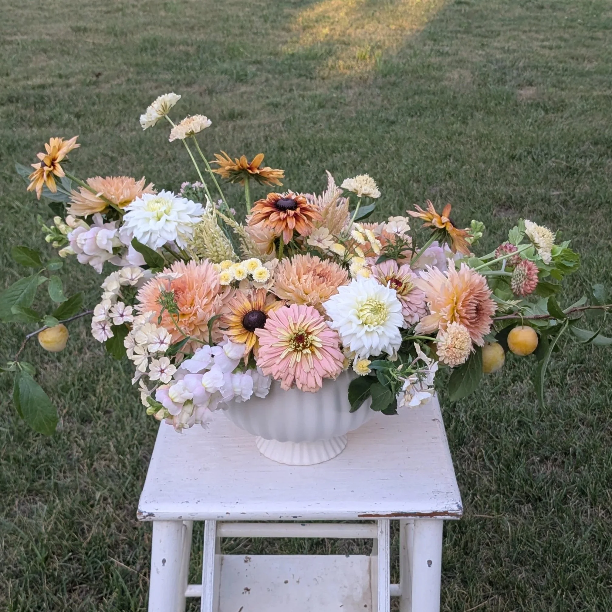 A colorful bouquet of mixed flowers in a white vase on a small white table outdoors on green grass.