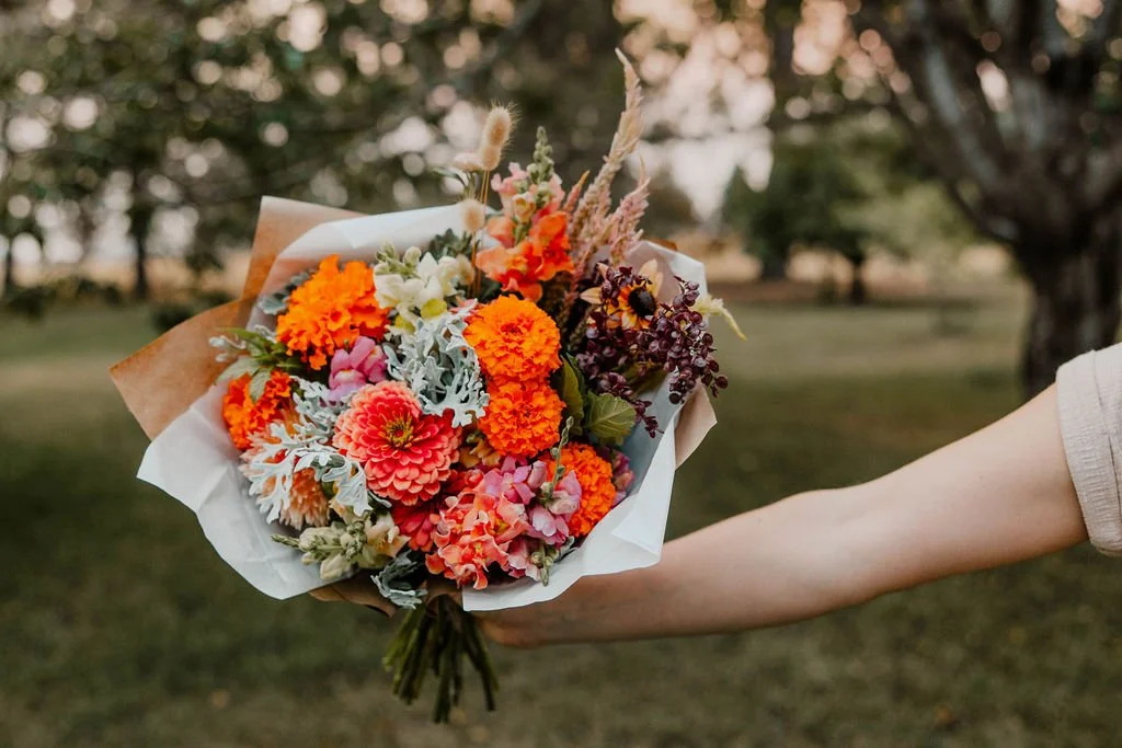 Person holding a colorful bouquet of flowers in an outdoor setting with trees in the background.