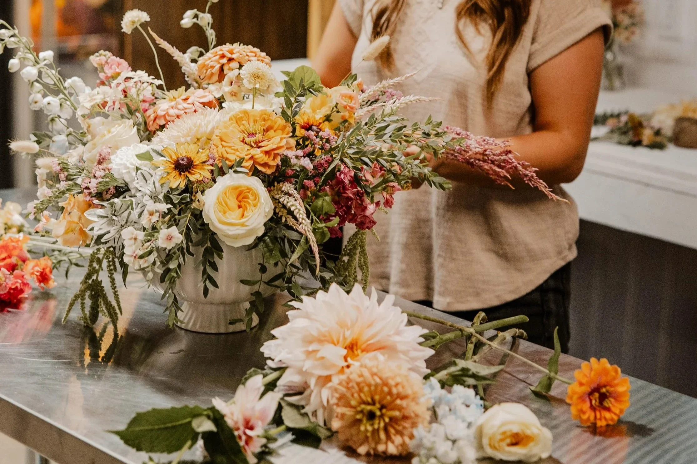 Woman arranging flowers in a indoor work area on a table with flowers laying next to a vase