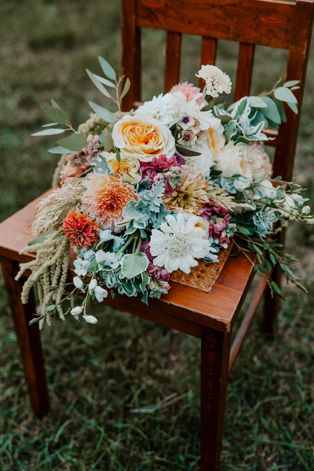A colorful floral arrangement with various flowers and greenery placed on a wooden chair outdoors.