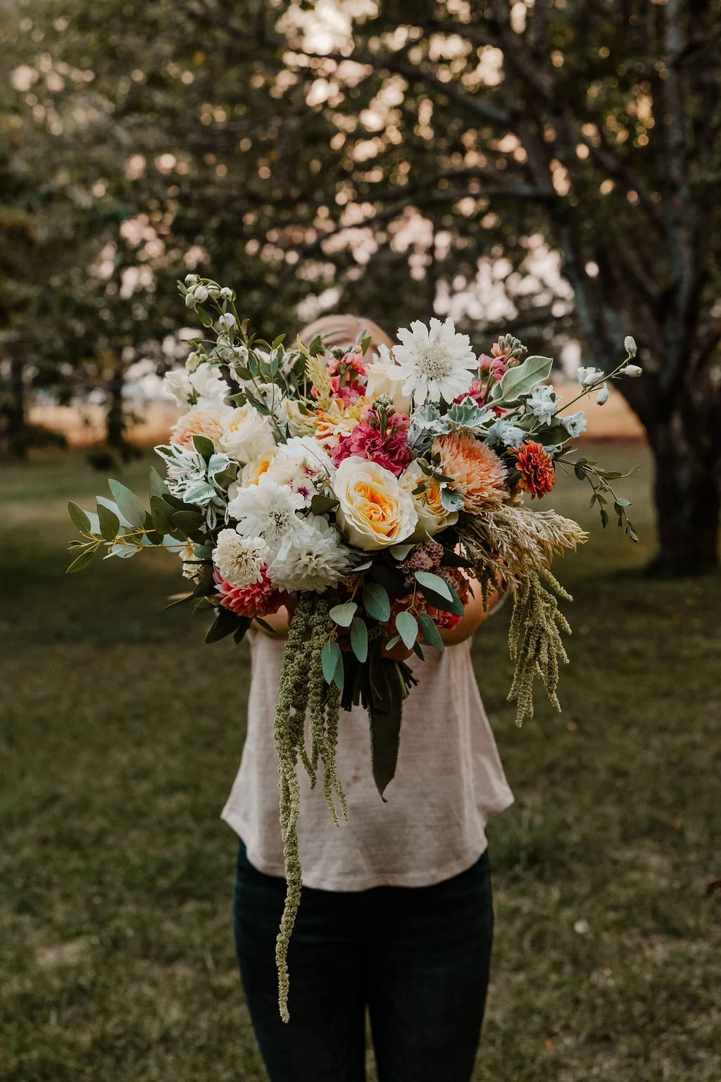 Woman holding a bridal bouquet in a park in pastel colors with roses, delphinium, and dahlias