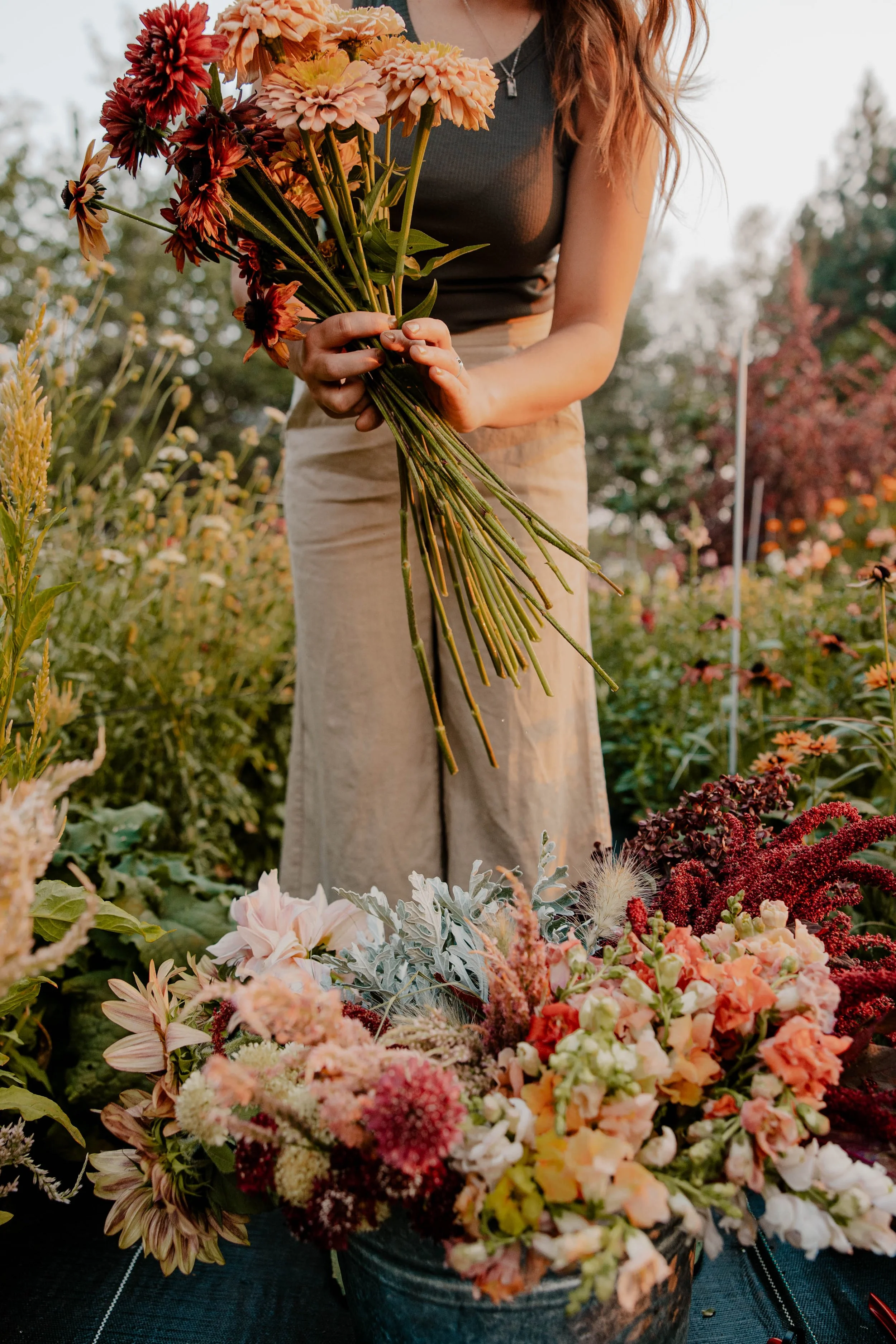 Person standing behind a bucket of flowers bending down with flowers in their hands.