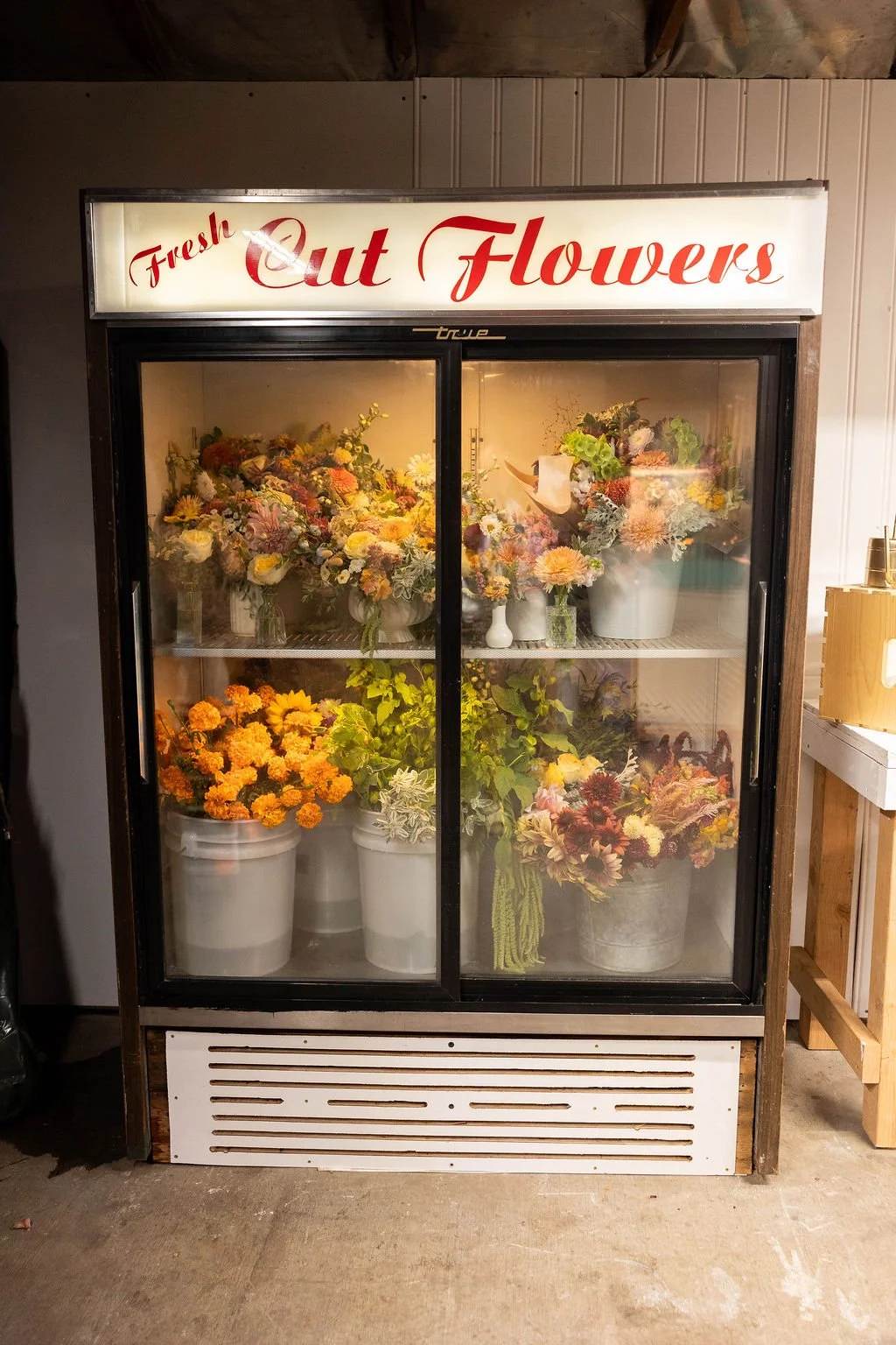 A refrigerated display case filled with various bouquets of fresh cut flowers in vases and buckets, with a sign above that reads 'Fresh Cut Flowers' in red script.