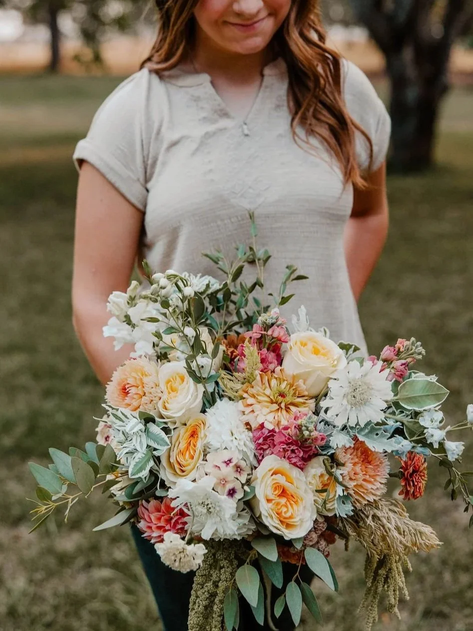 Person holding a large bouquet of mixed flowers including roses outdoors in a park