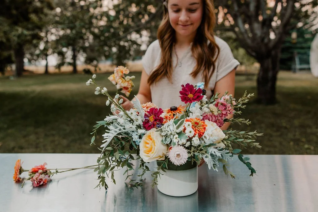 Young woman arranging a colorful flower bouquet in a white vase outdoors.