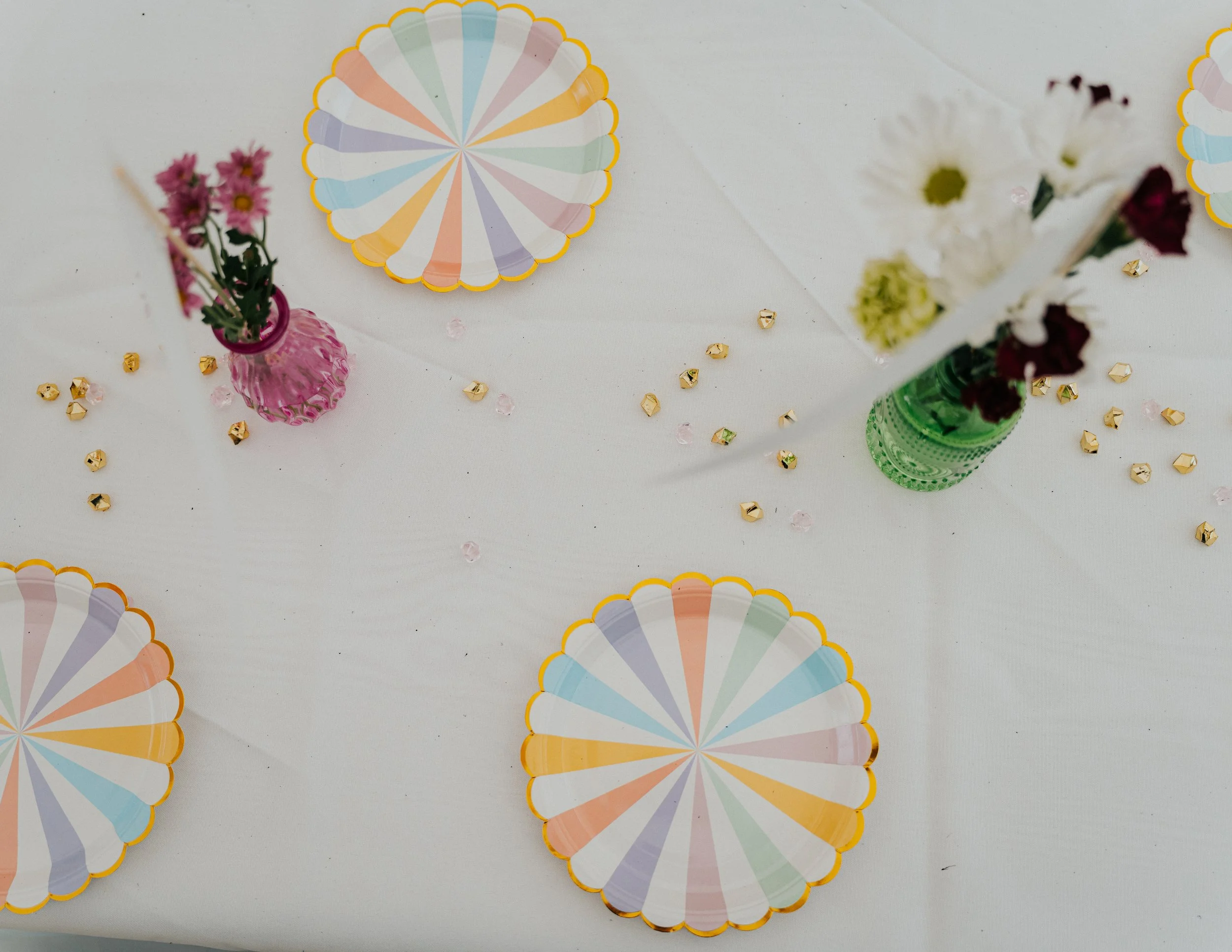 Colorful paper fans, vases with flowers, and scattered small decorative items on a white table.
