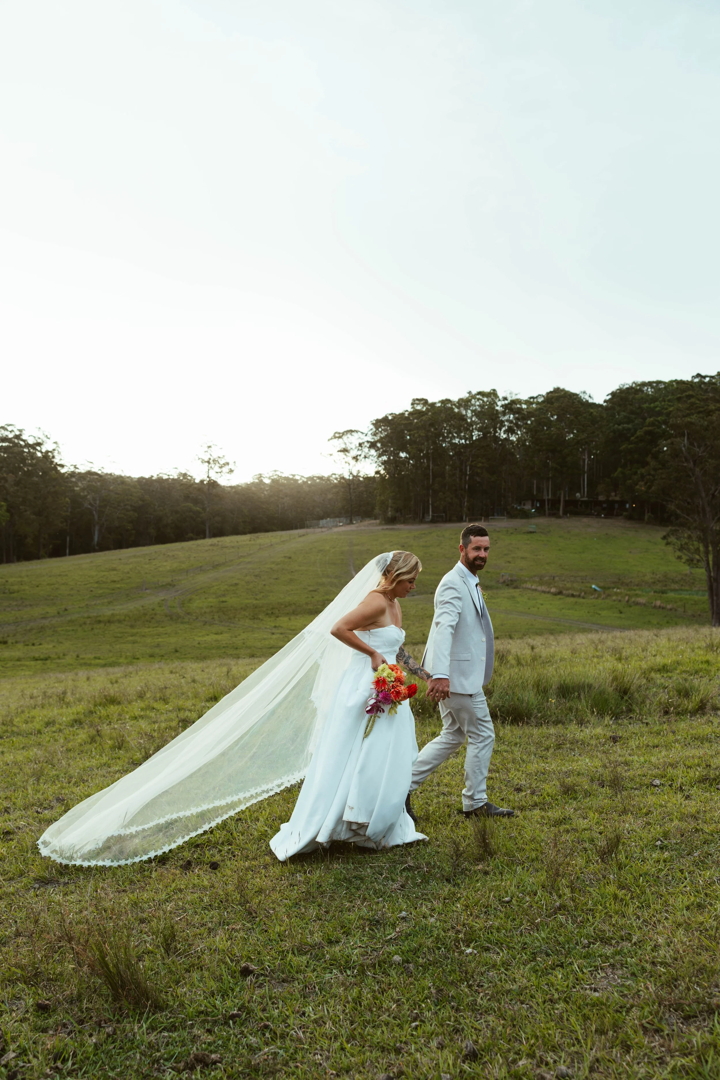 Bride and groom walking hand in hand through a field at sunset, Barrington Coast wedding