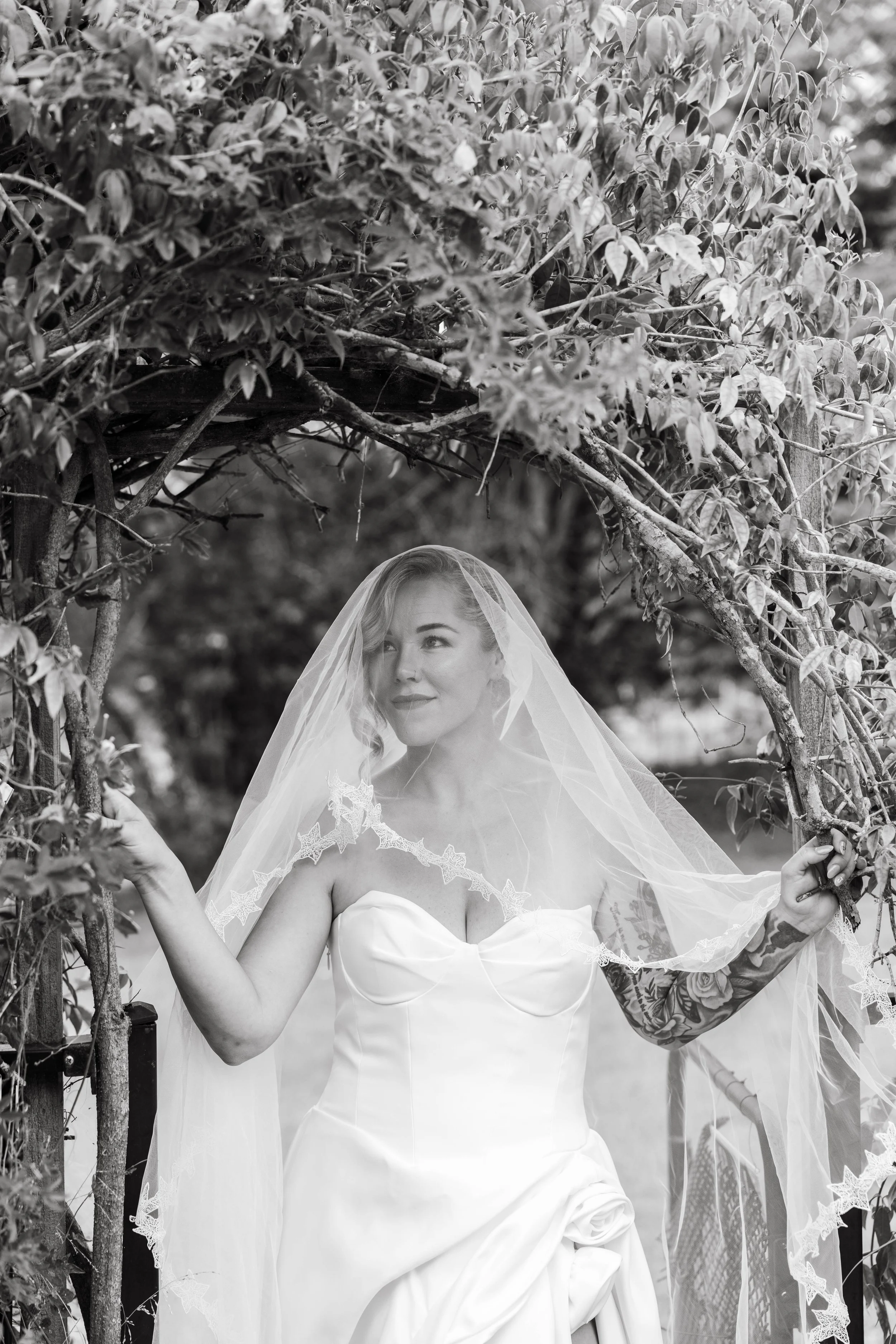 Bride smiling beneath a vine-covered arbour, black and white wedding portrait, Mid North Coast NSW