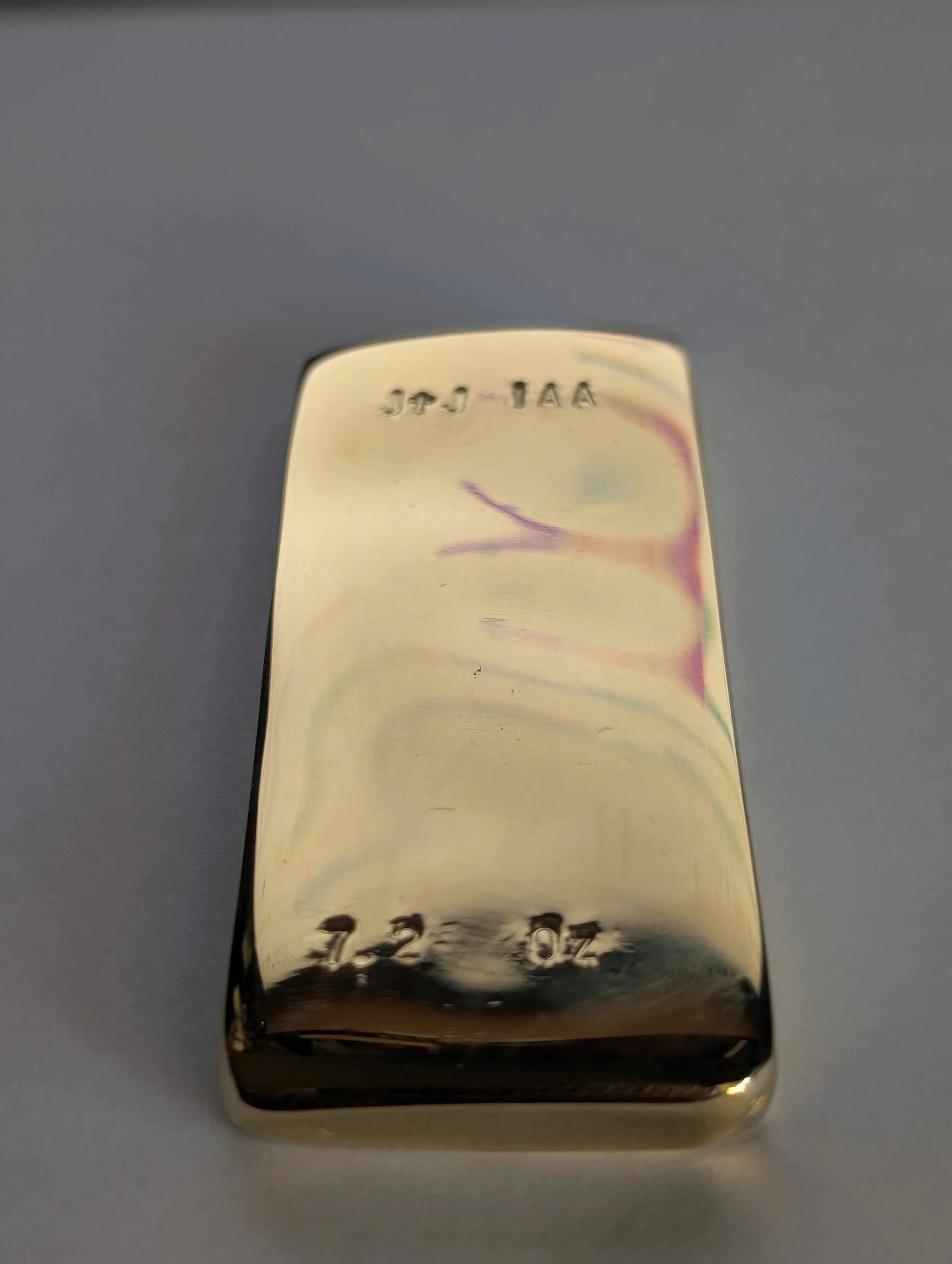 Refined gold ingot with stamped markings on top and bottom, resting on a smooth surface.