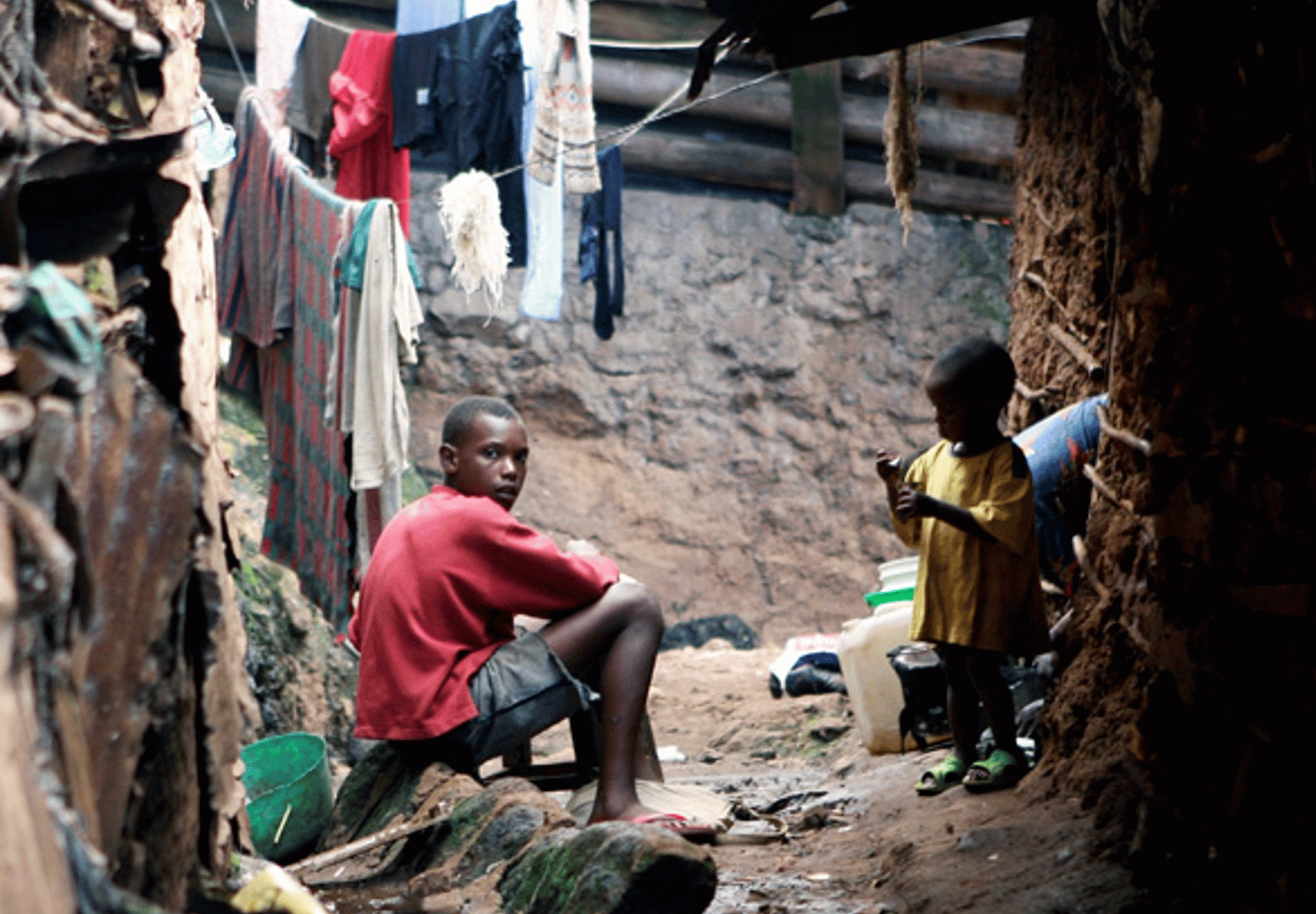 Teenaage boy and toddler sitting amongst hanging laundry on rocks
