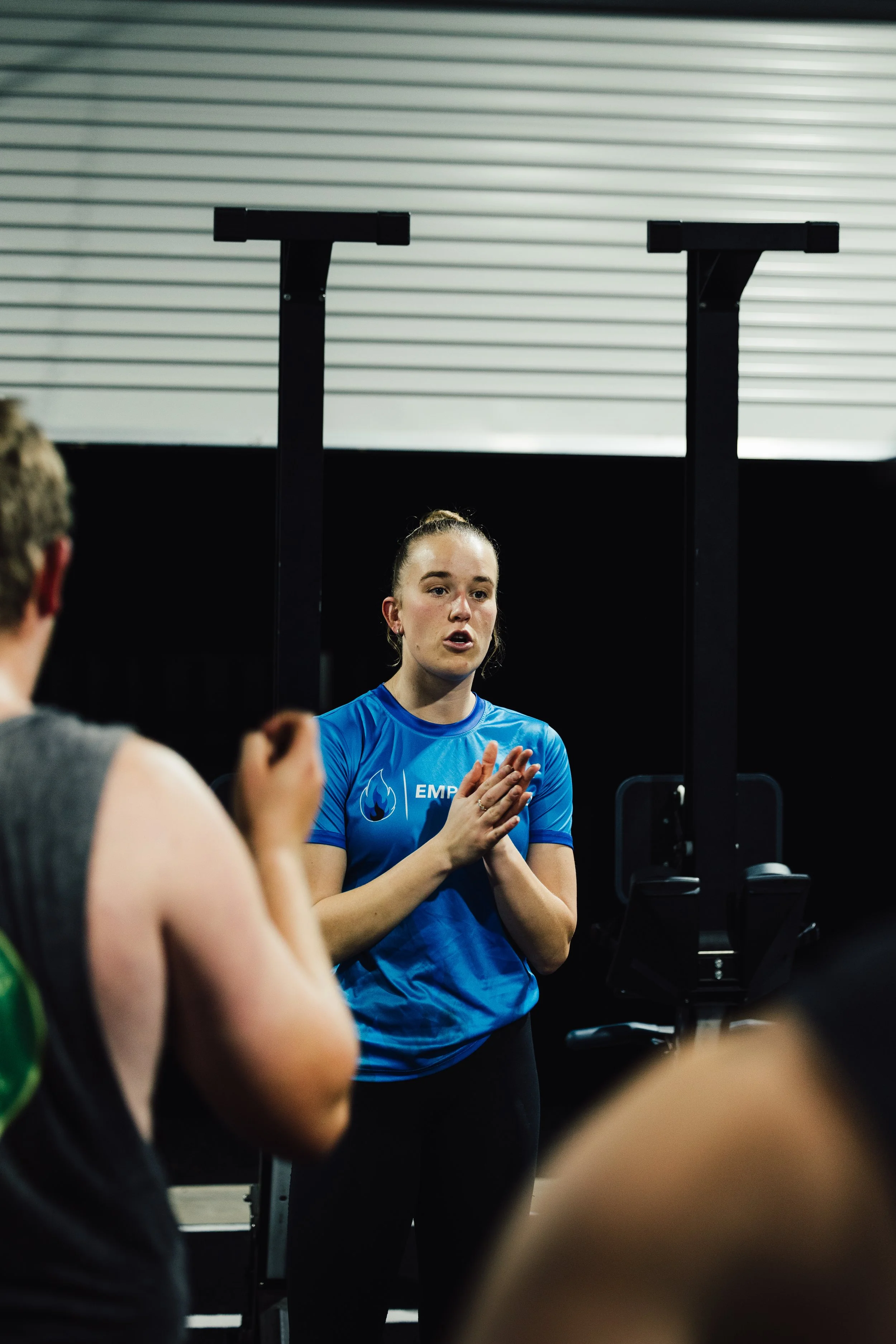 Female fitness instructor speaking to a group of athletes inside gym.