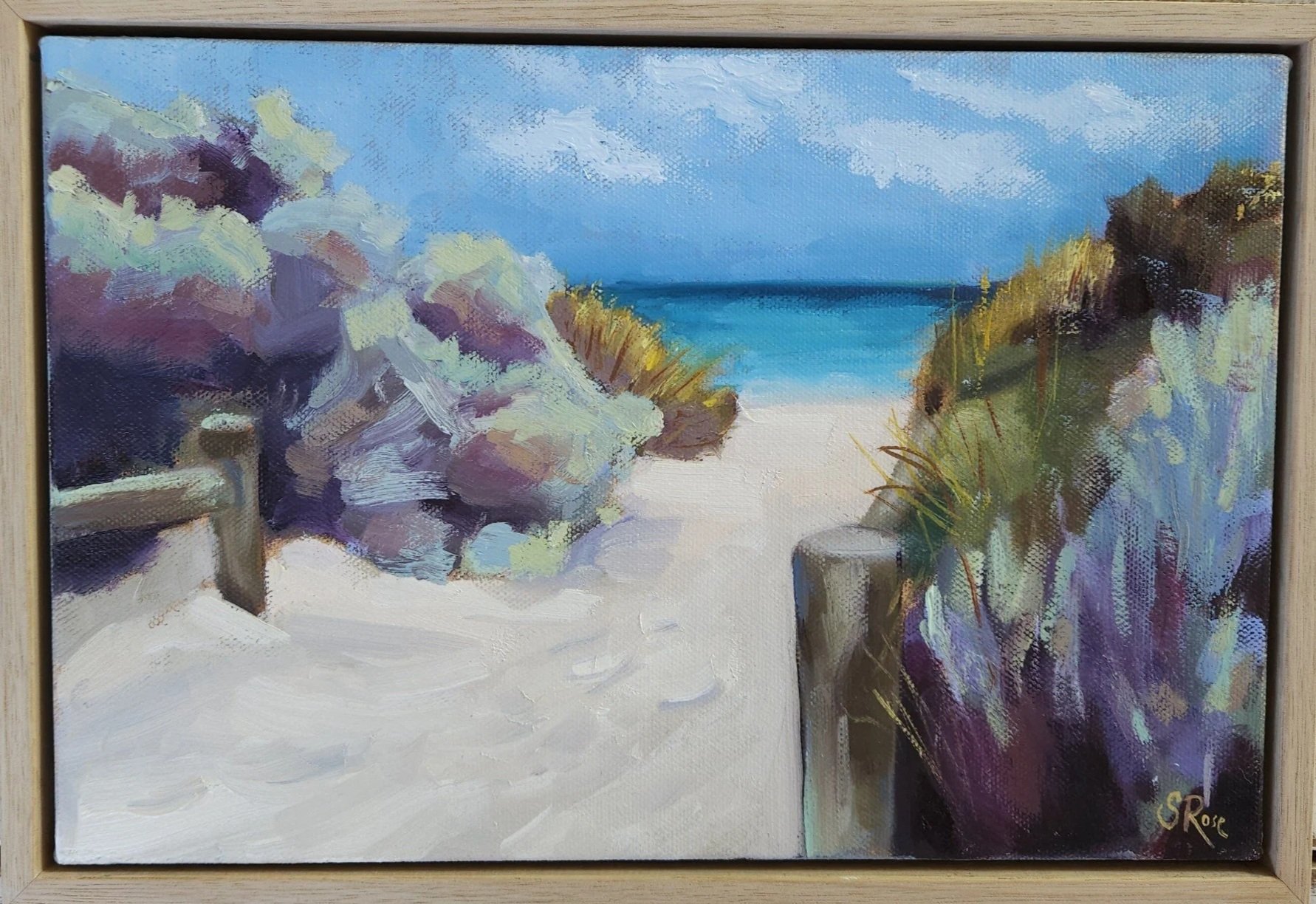 An oil painting of a sandy beach with dune grasses and colorful shrubbery, leading to blue ocean water and a partly cloudy sky.
