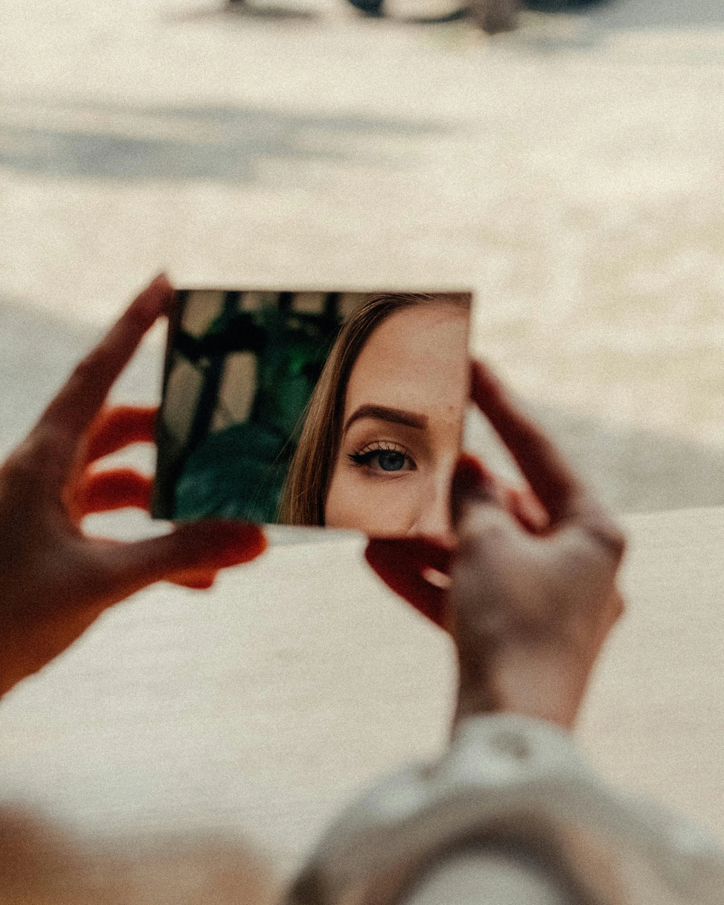 A person holding a mirror in front of their face, reflecting their eye and eyebrow with a background of trees.