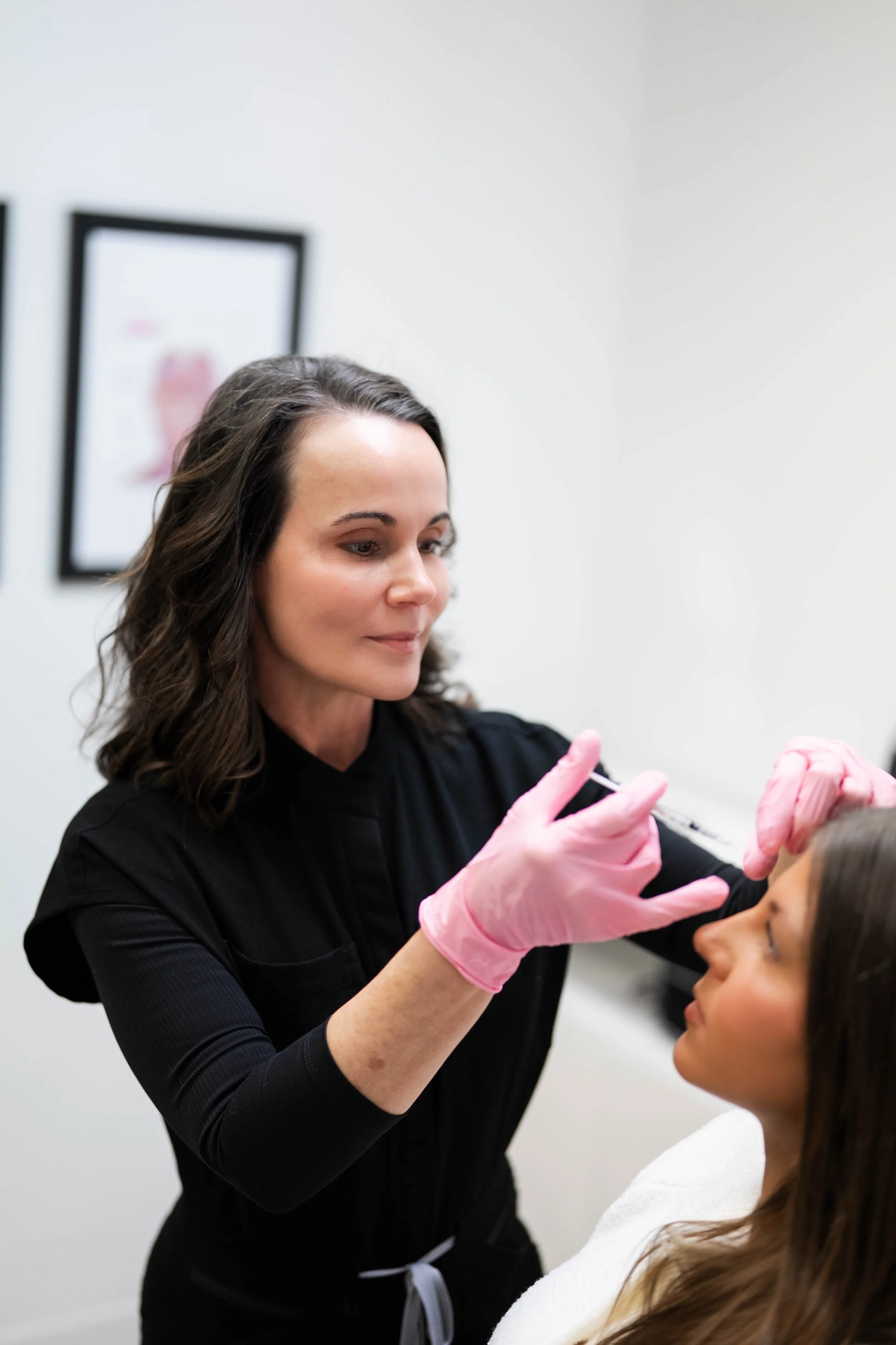 A woman is receiving an injection in her forehead from a medical professional wearing pink gloves.