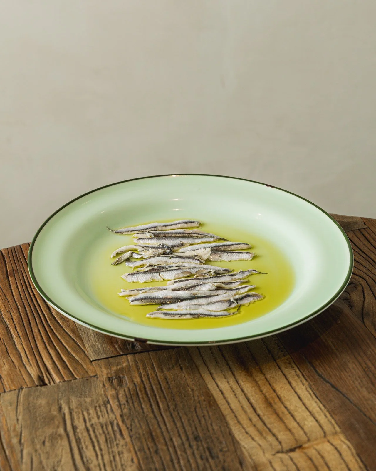 Small dried fish in olive oil on a light green plate placed on a wooden table.