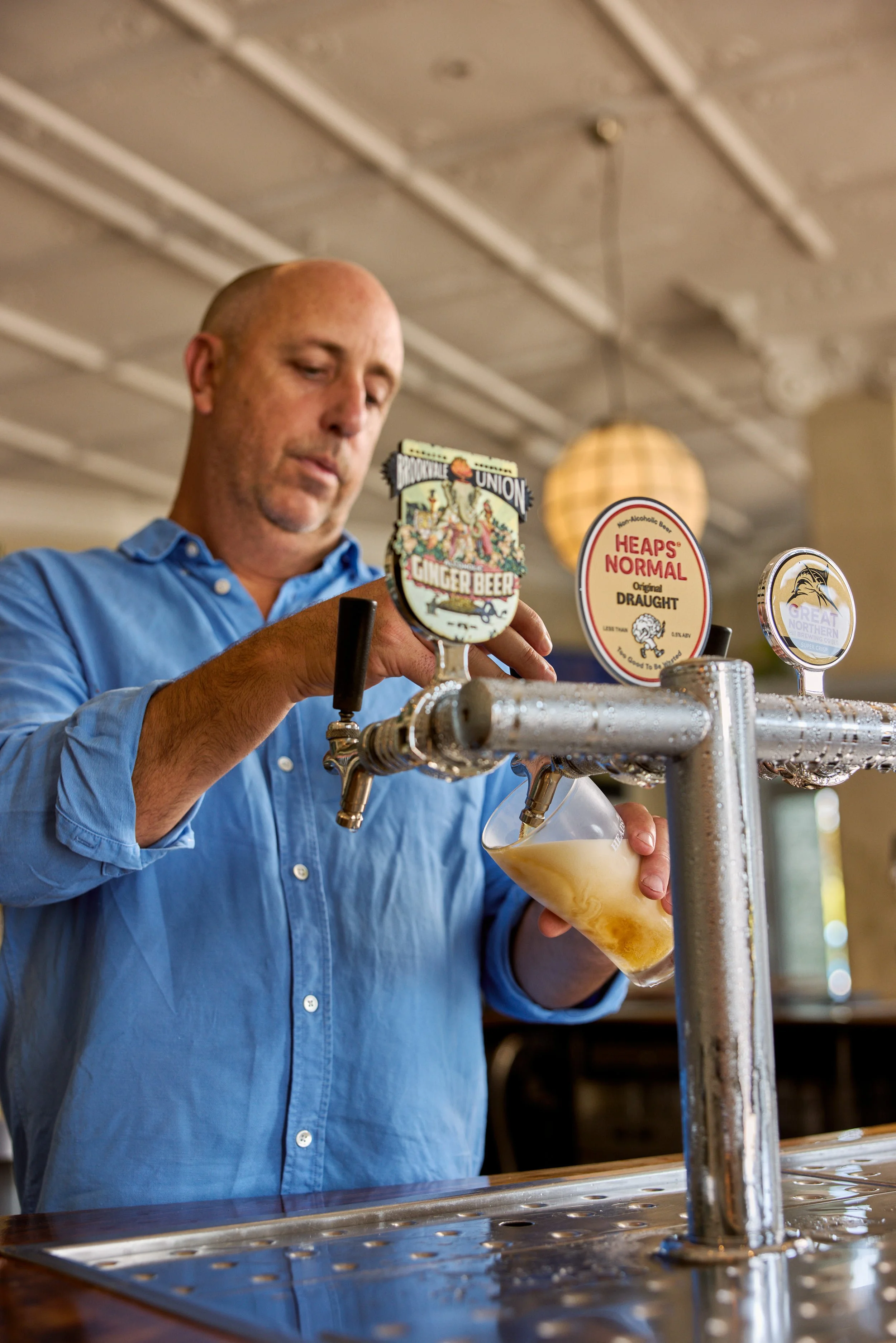 A man in a blue shirt pours beer from a tap into a glass at a bar.