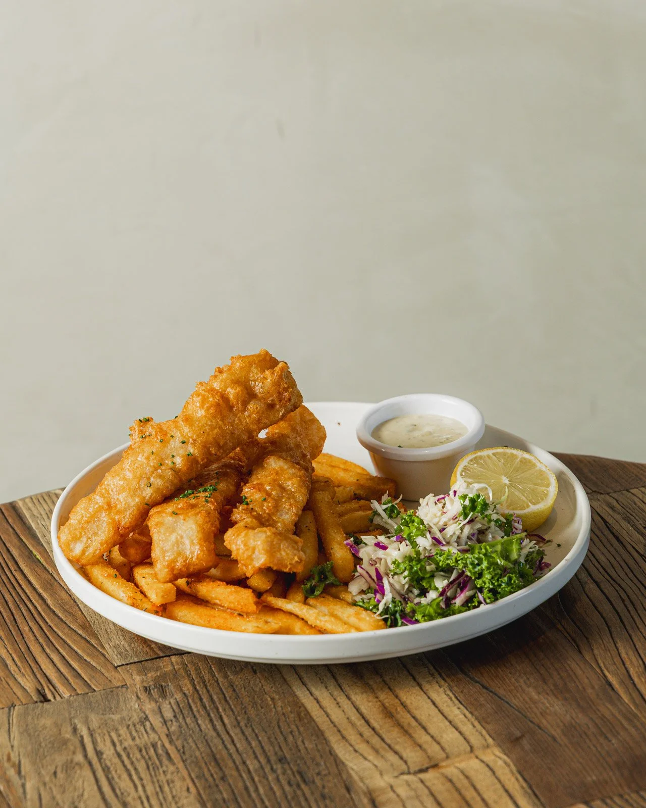 Fried fish, French fries, coleslaw, lemon wedge, tartar sauce on a white plate.